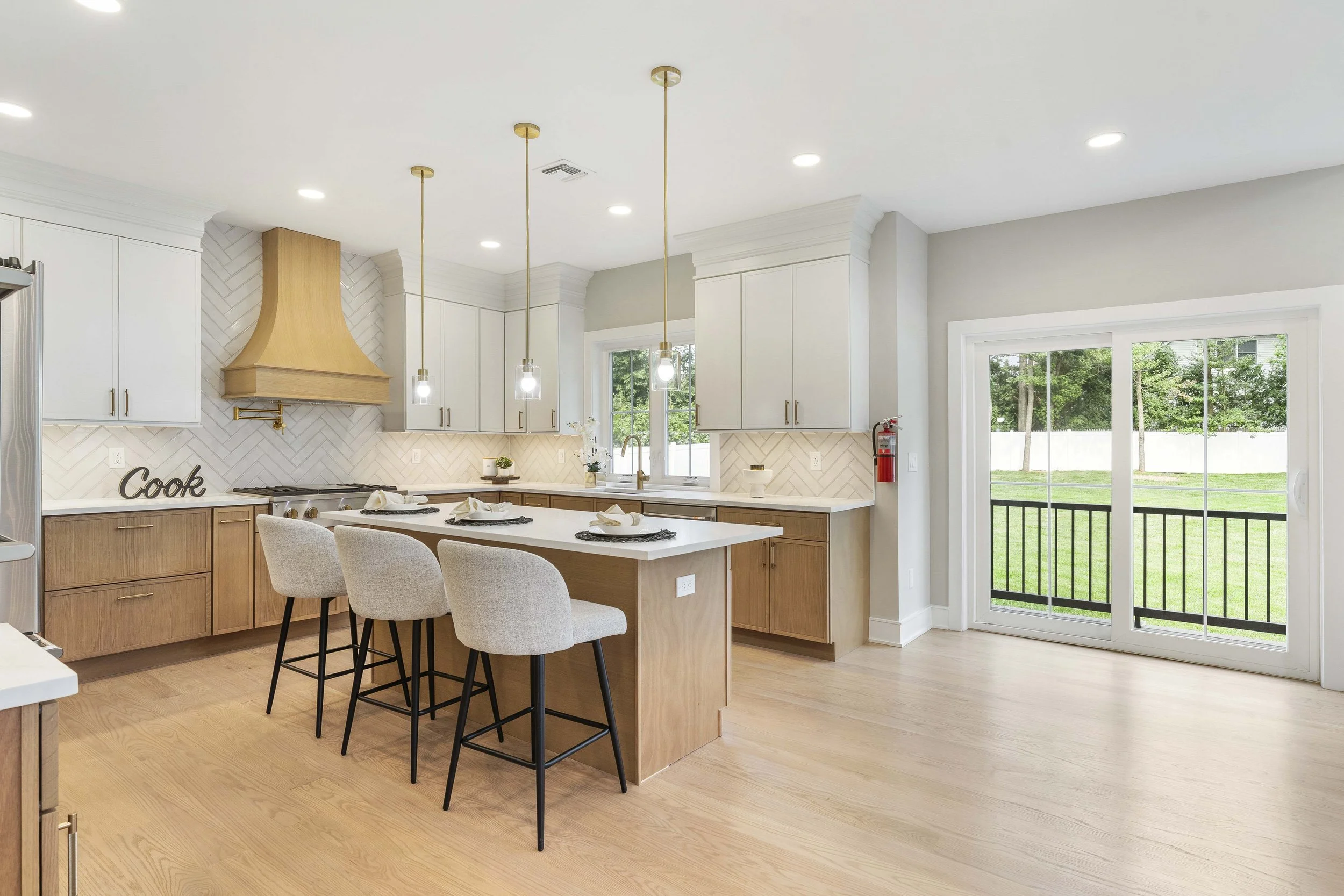 Bright kitchen with white and wood cabinets, a kitchen island with four beige chairs, and sliding glass doors leading outside to a green yard.
