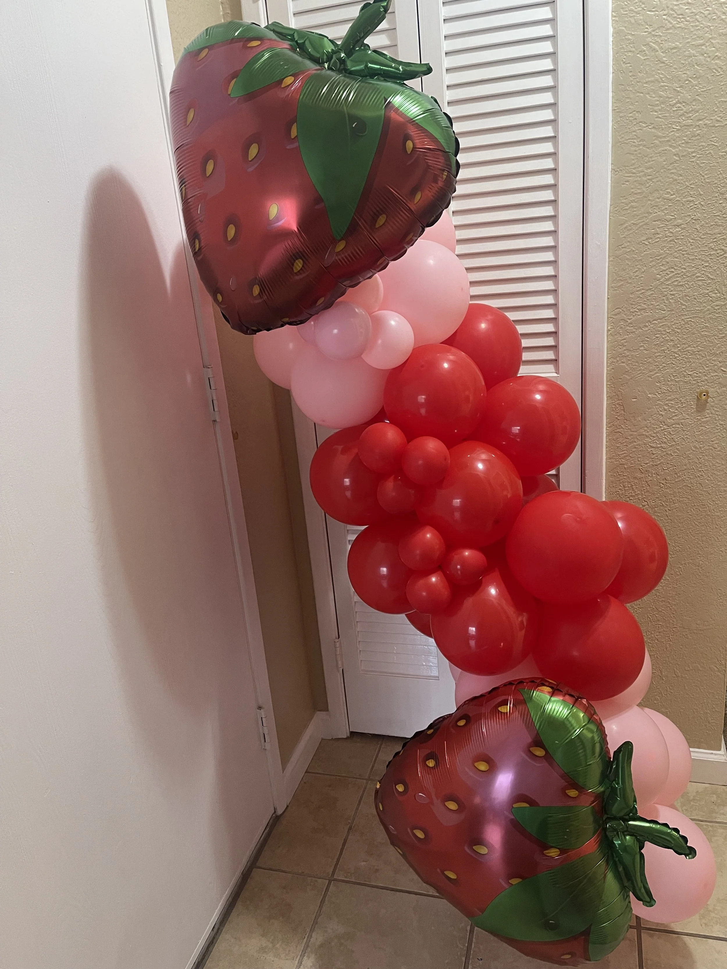 A large wall of numerous white roses with green leaves at the bottom, with a woven mat on the floor in the foreground.