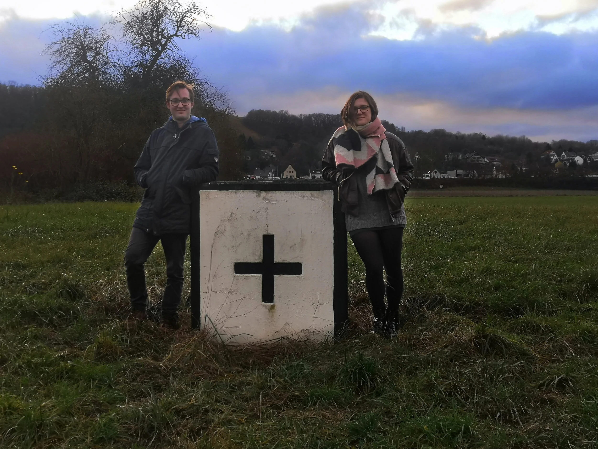 Florian Becht und Anke Ulbrich stehen auf einer Wiese. Sie lehnen an einem Betonwürfel, auf dem ein Plus zu sehen ist.