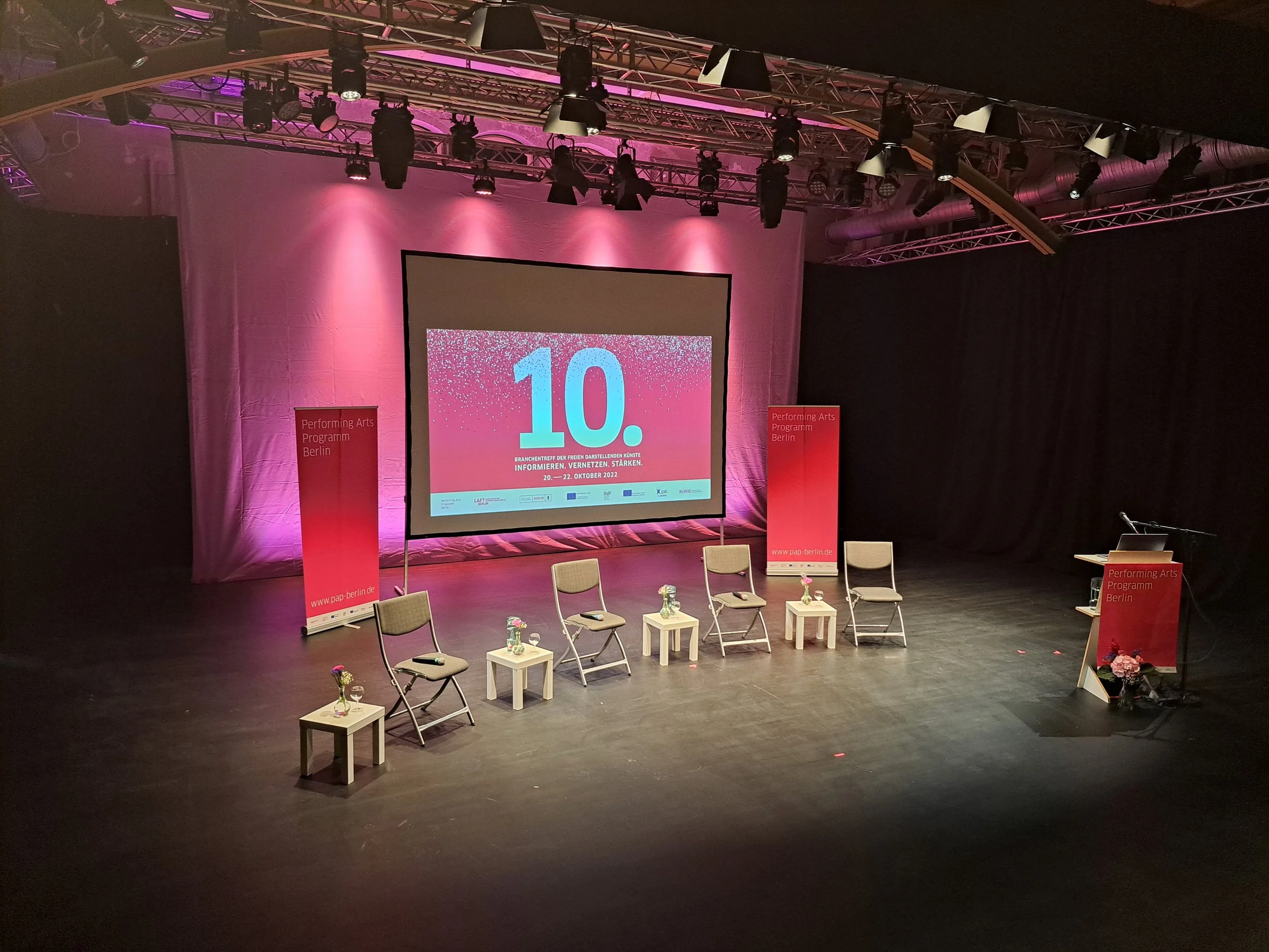 Die Bühne ist bereit für den 10. Branchentreff. Das Bühnendesign ist in pink gehalten, die vier leeren Stühle warten auf die Podiumsgäste.