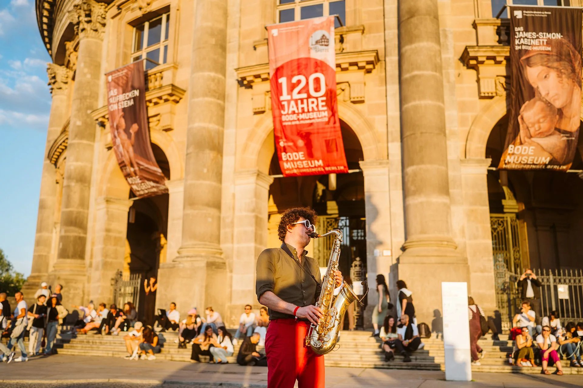 Ein Saxophonist spielt bei strahlendem Sonnenschein vor dem Bode-Museum.