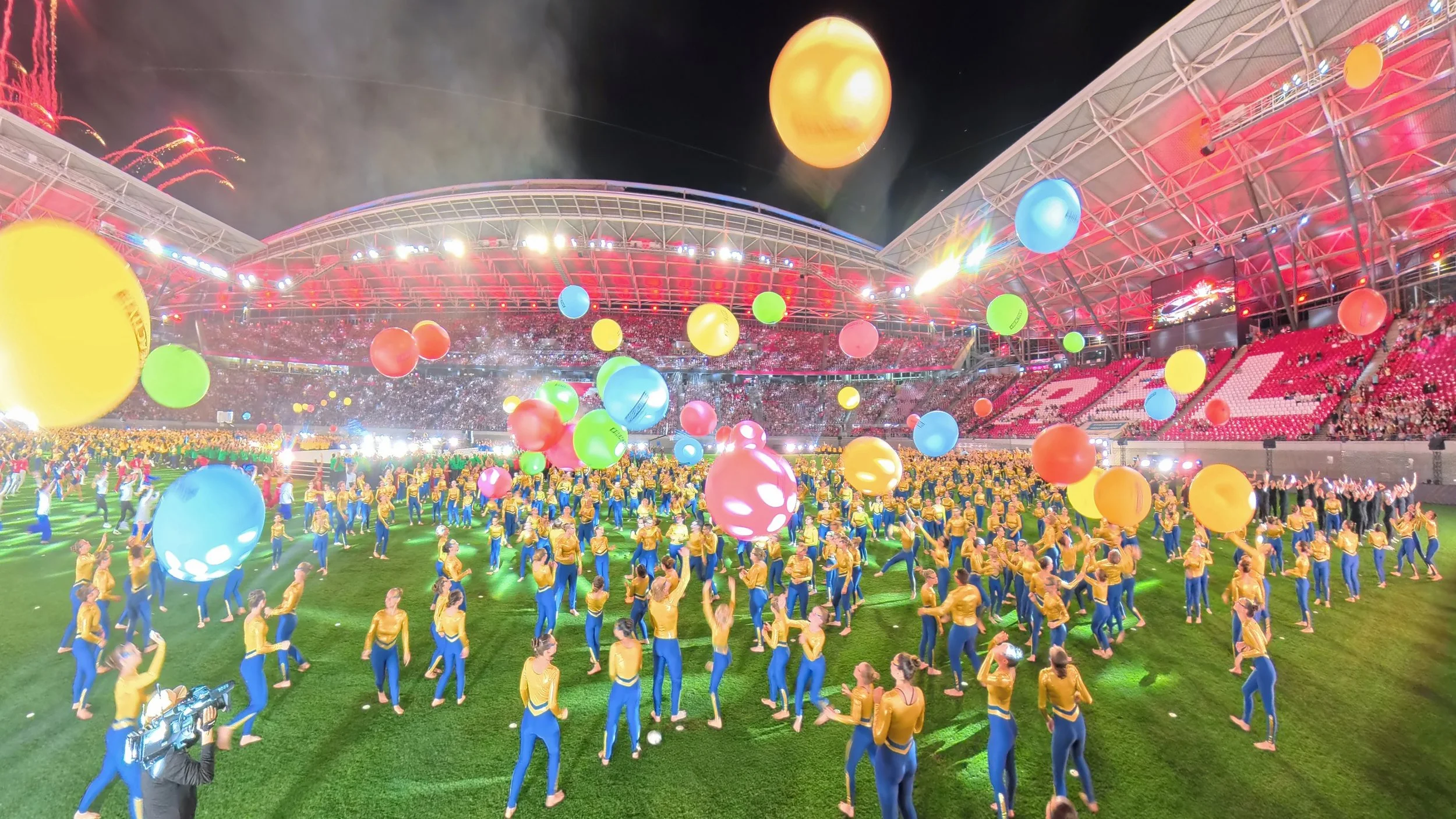 Choreografie mit über 1000 Turner*innen. Es werden viele bunte, große Bälle in die Luft geworfen.