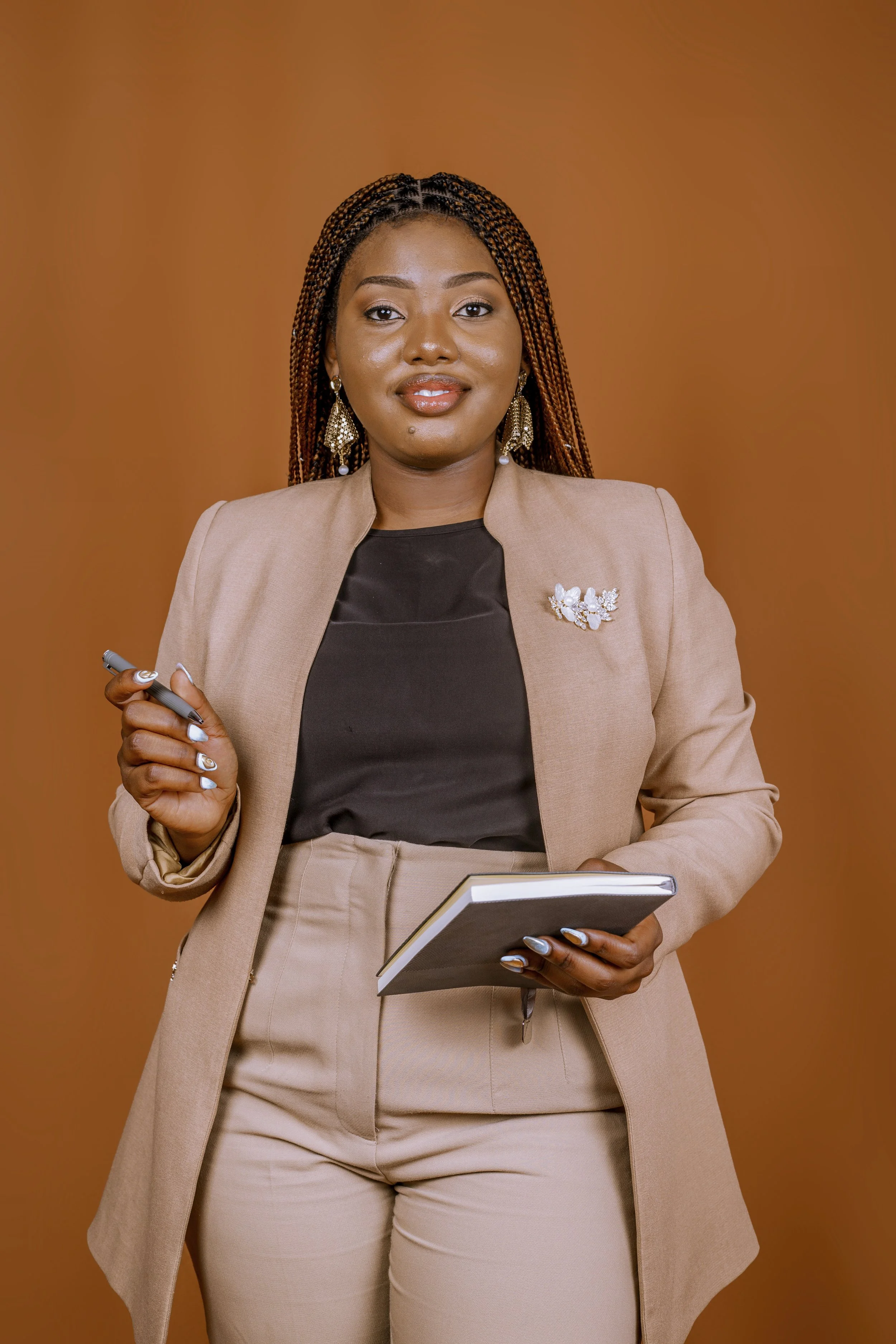 A professional woman with long braided hair, wearing a beige blazer and pants, holding a tablet and a pen, standing against an orange background.