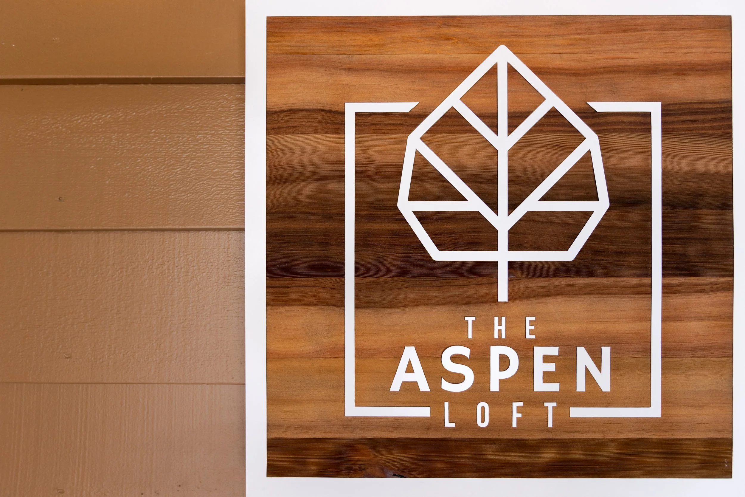 Sign for The Aspen Loft with a geometric leaf logo on wood background.