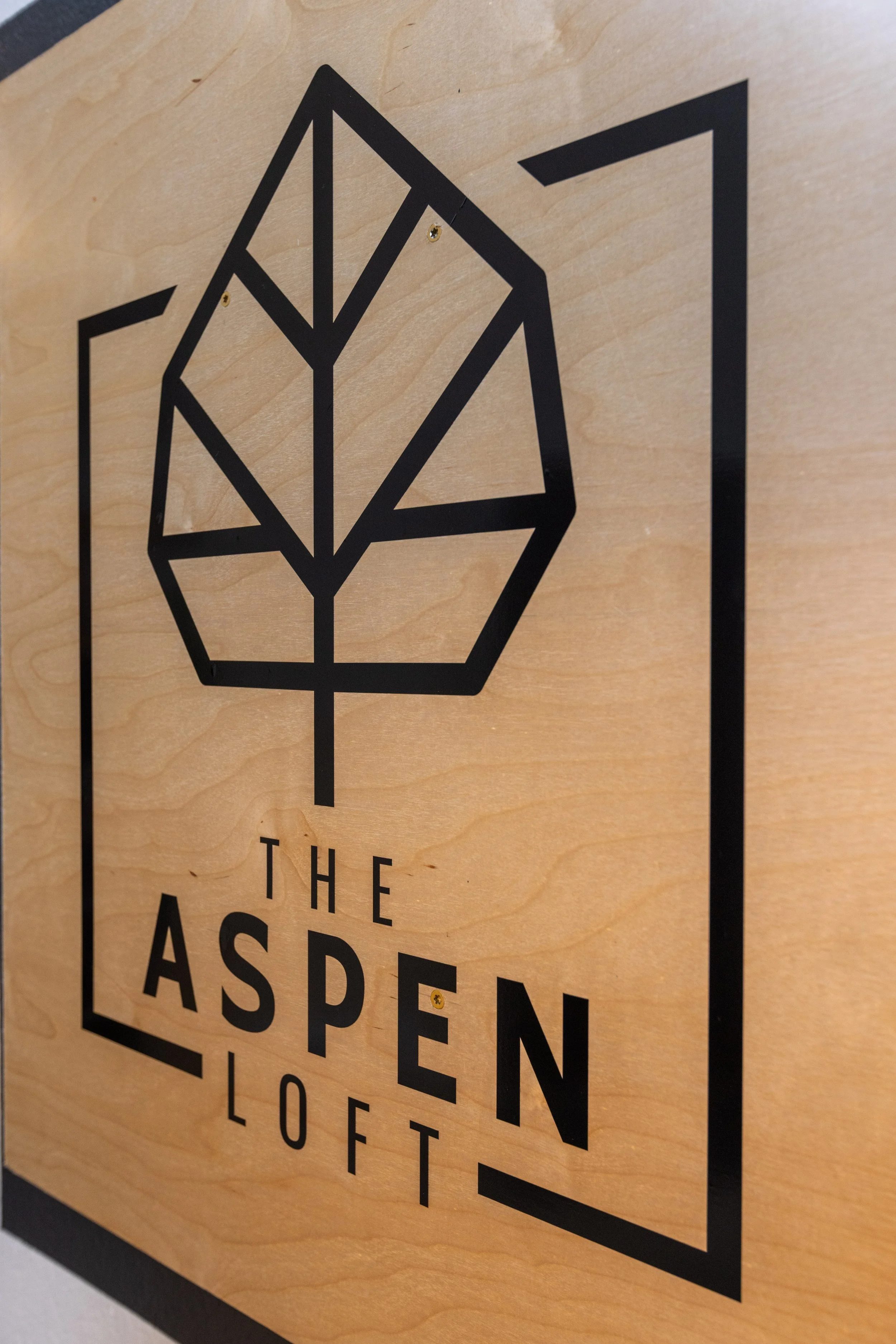 A black geometric tree logo with the words "The Aspen Loft" on a wooden background.