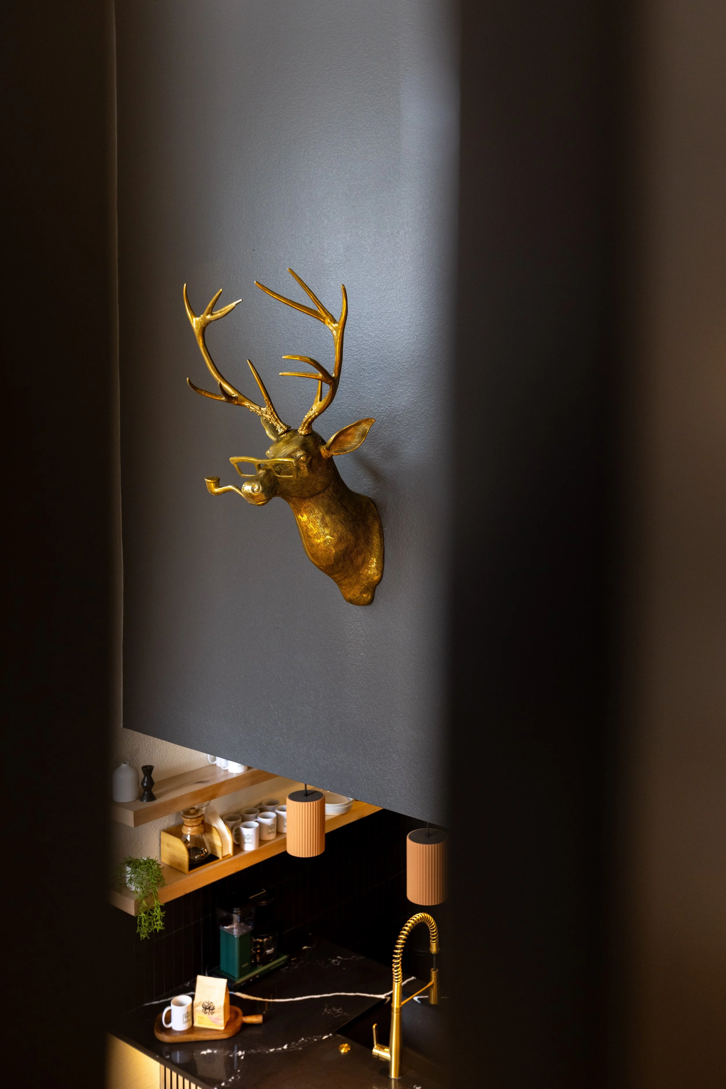 Decorative golden deer head mounted on a gray wall in a modern kitchen with black marble countertop and gold fixtures.