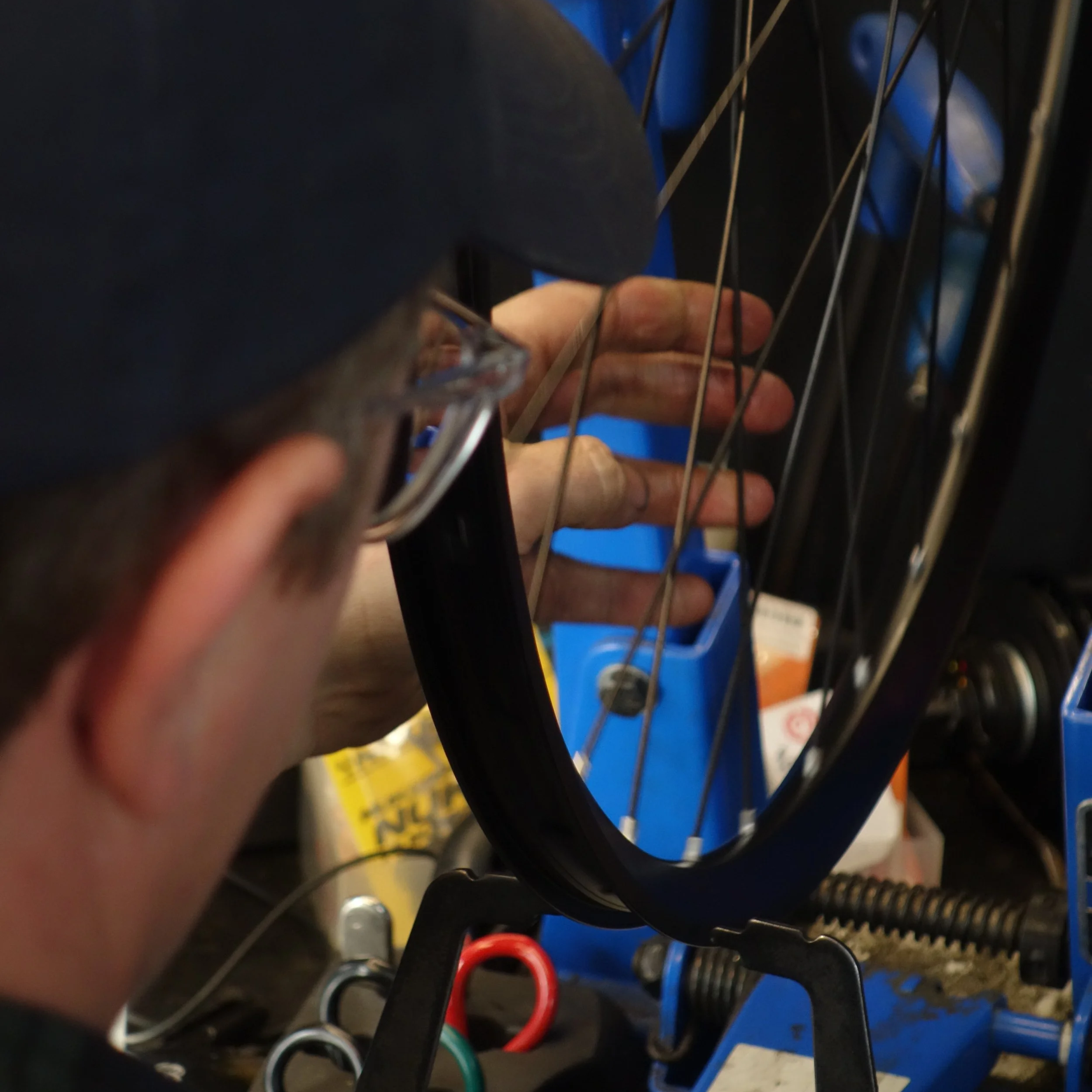 Close-up of a person working on a bicycle wheel, adjusting or repairing it with tools, in a workshop.
