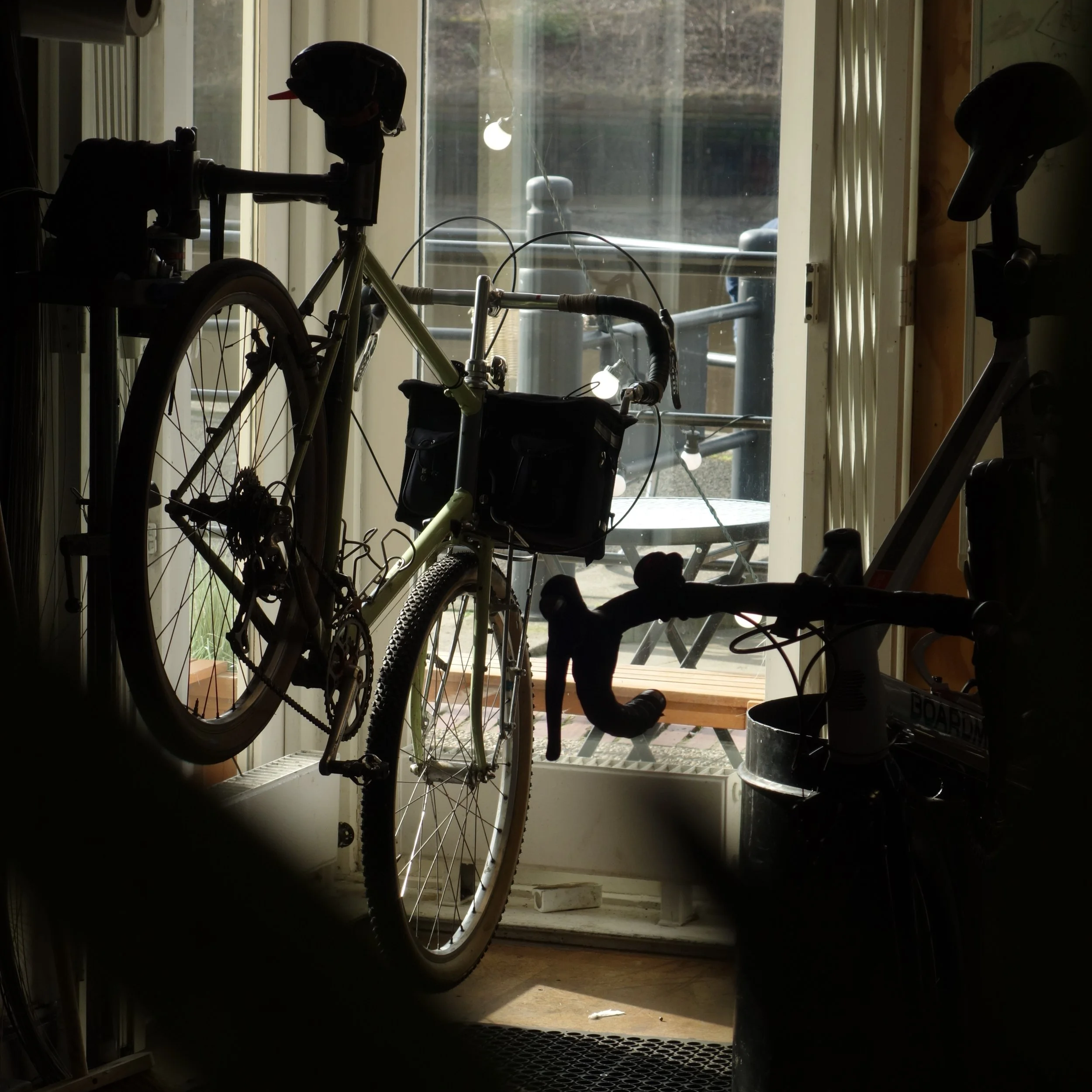 Two bicycles inside a house near a glass door, with an outdoor patio visible through the door.
