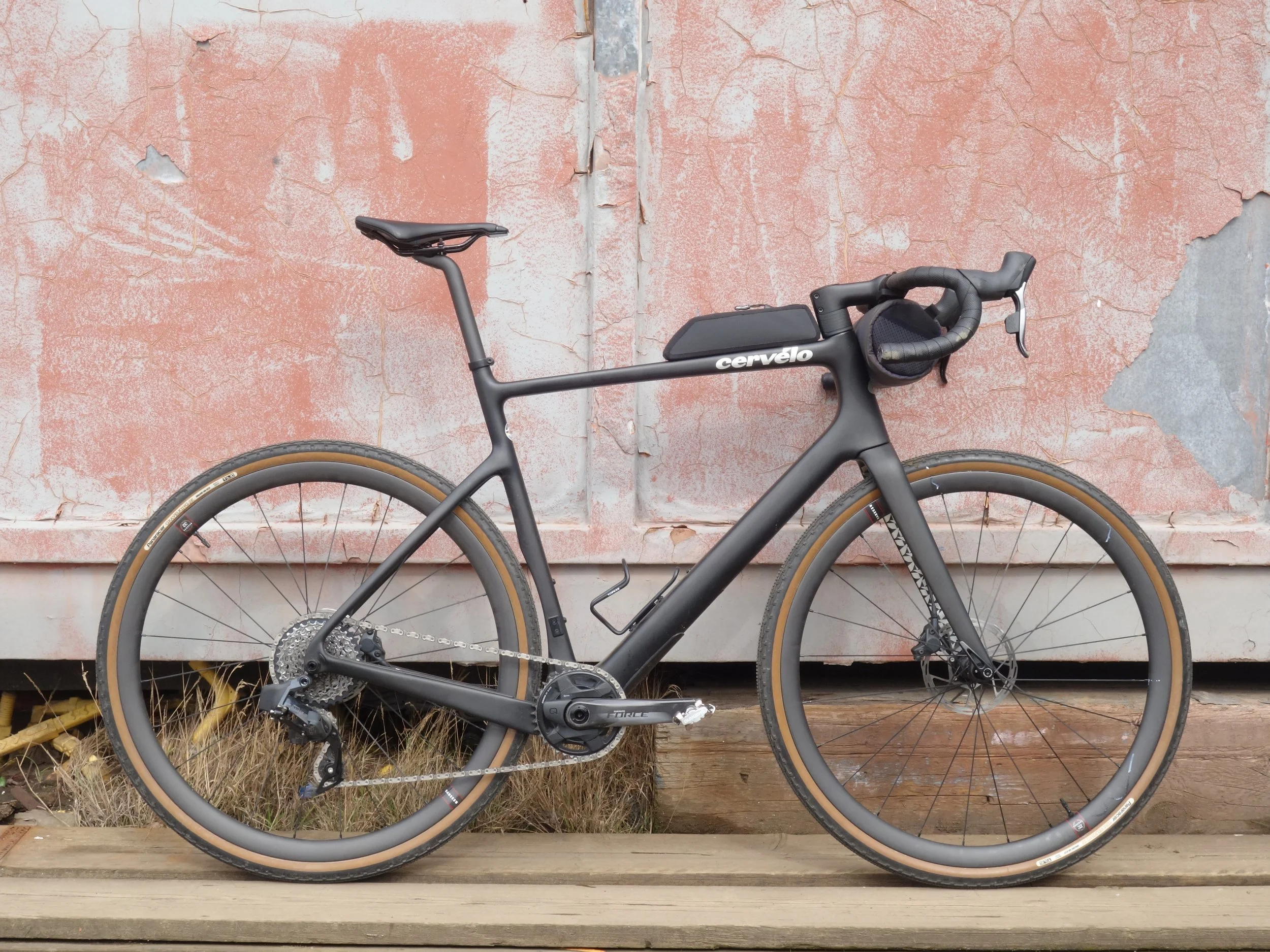 Black road bicycle with brown tires leaning against a weathered pink and gray wall.