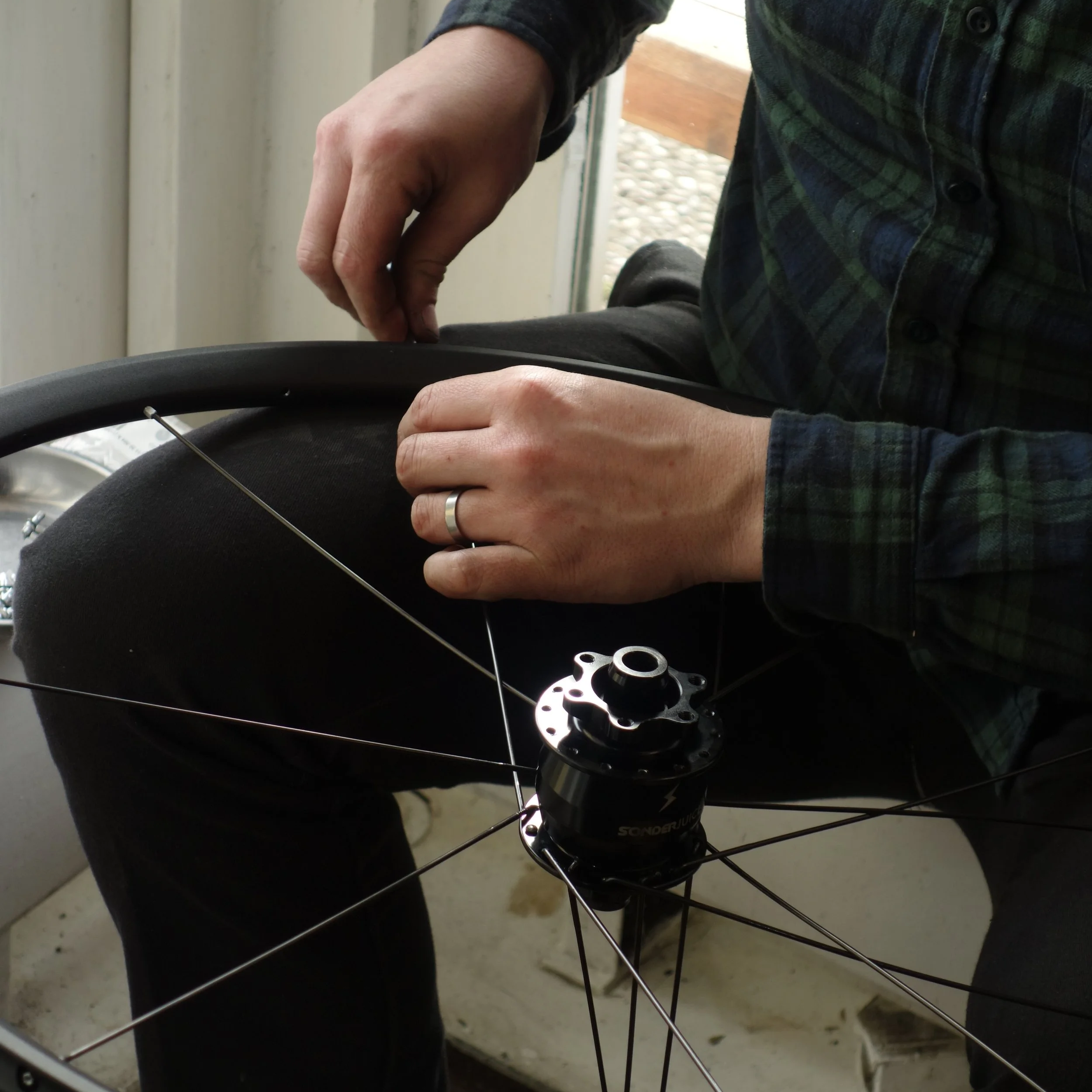 A person inspecting or repairing a bicycle wheel, focusing on the hub and spokes.