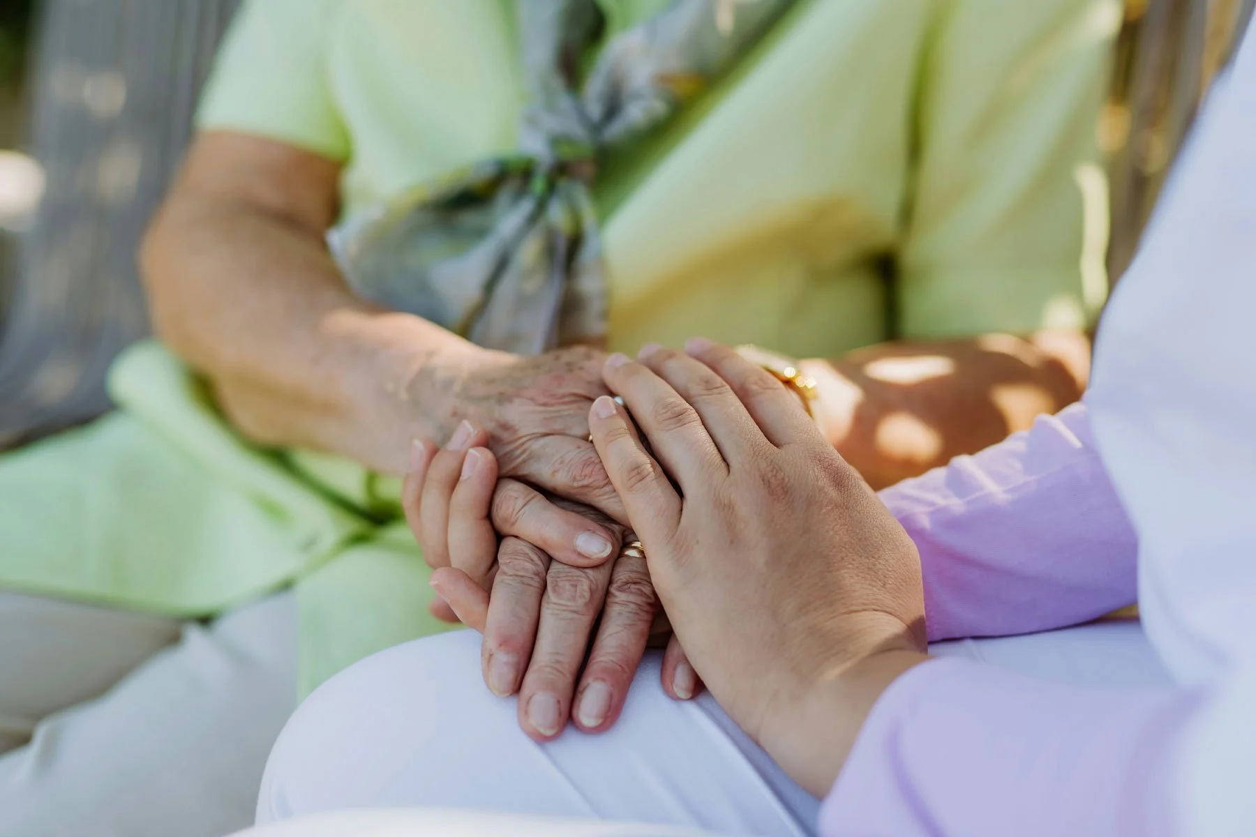 A caregiver holds an older adult's hand during a senior companionship care visit.