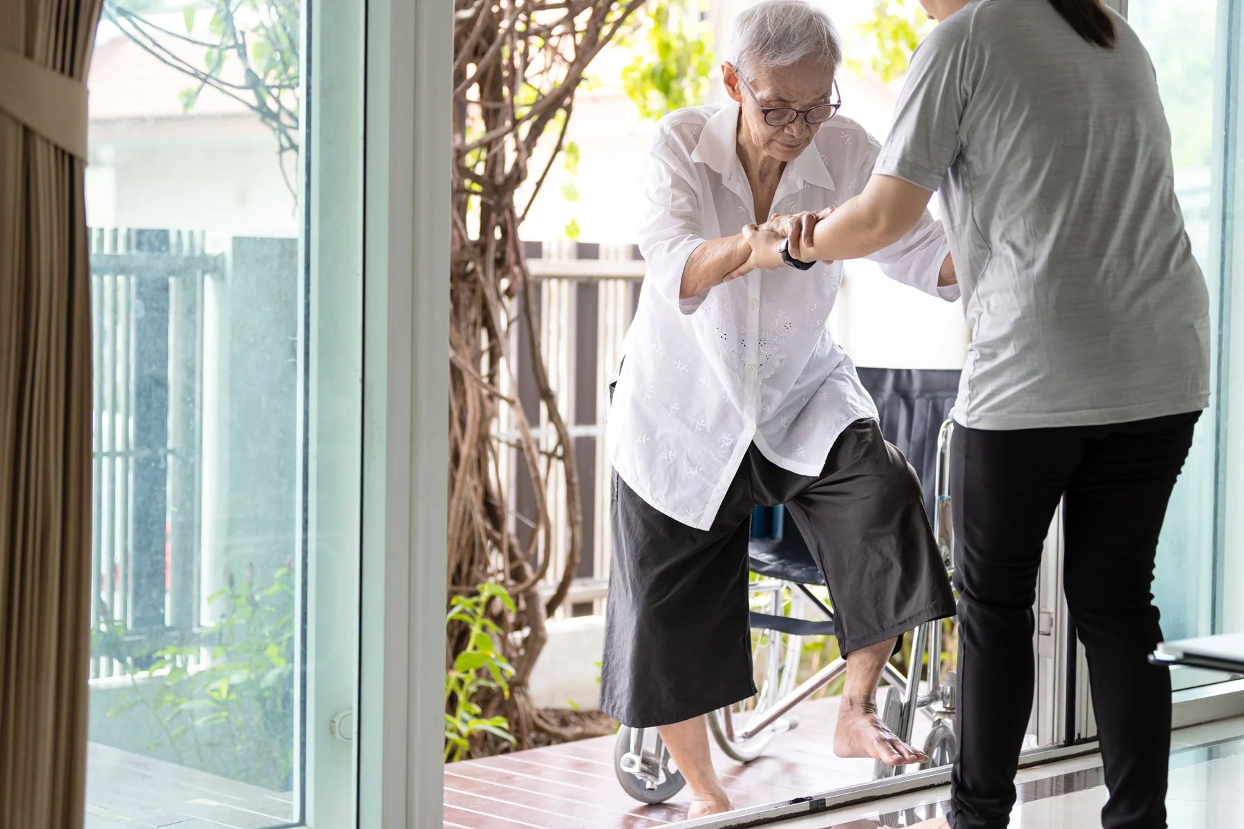 A caregiver helps an older adult step up safely during an in-home care visit.
