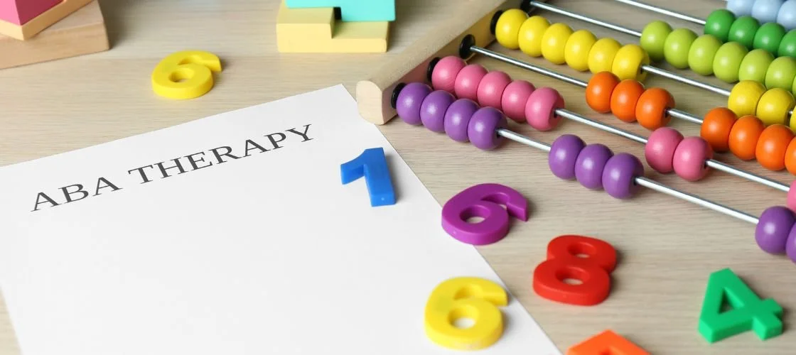 Colorful numbers and an abacus on a light wooden table, with a paper labeled 'ABA THERAPY'.
