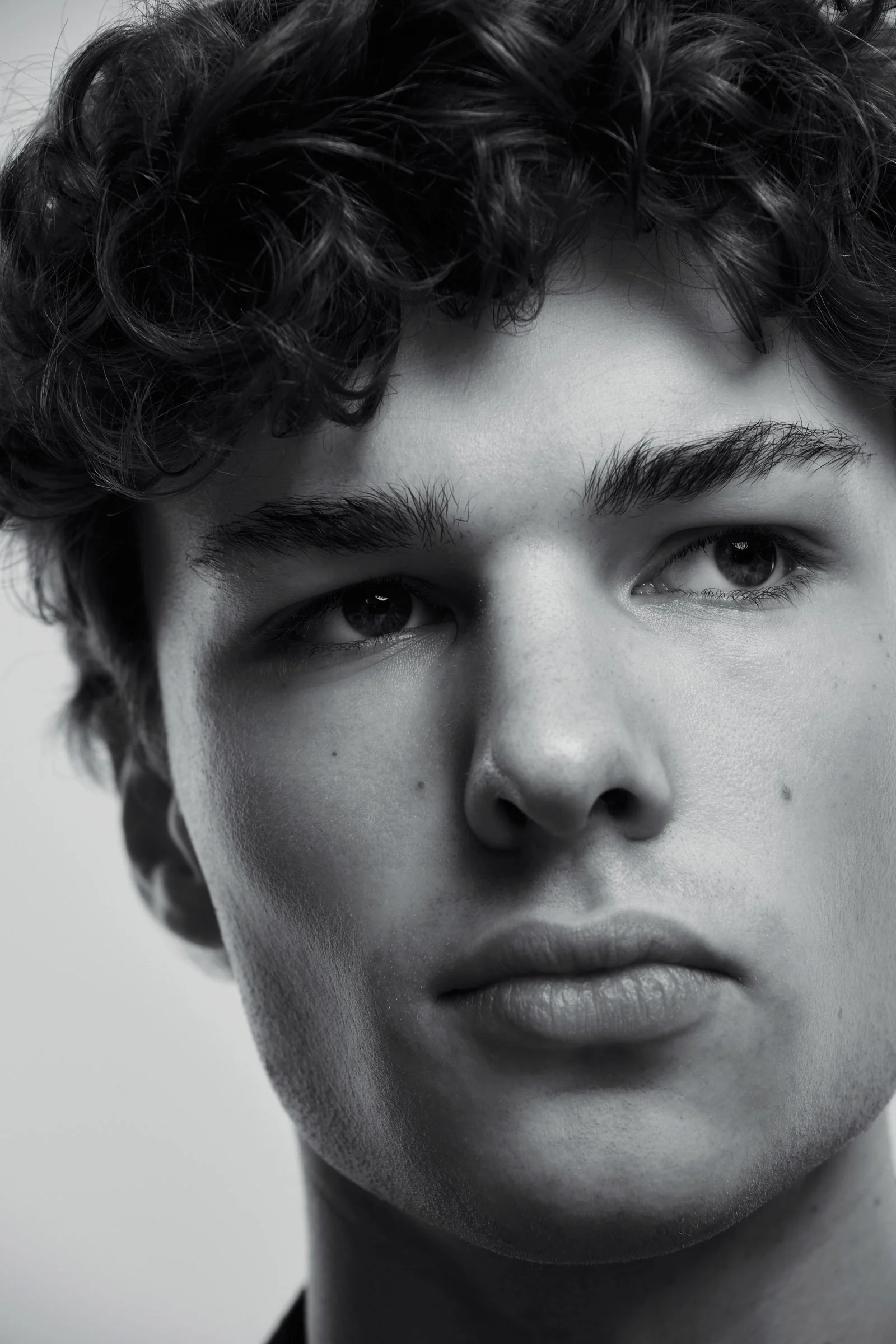 A close-up black and white portrait of a young person with curly hair, full lips, and expressive eyes.