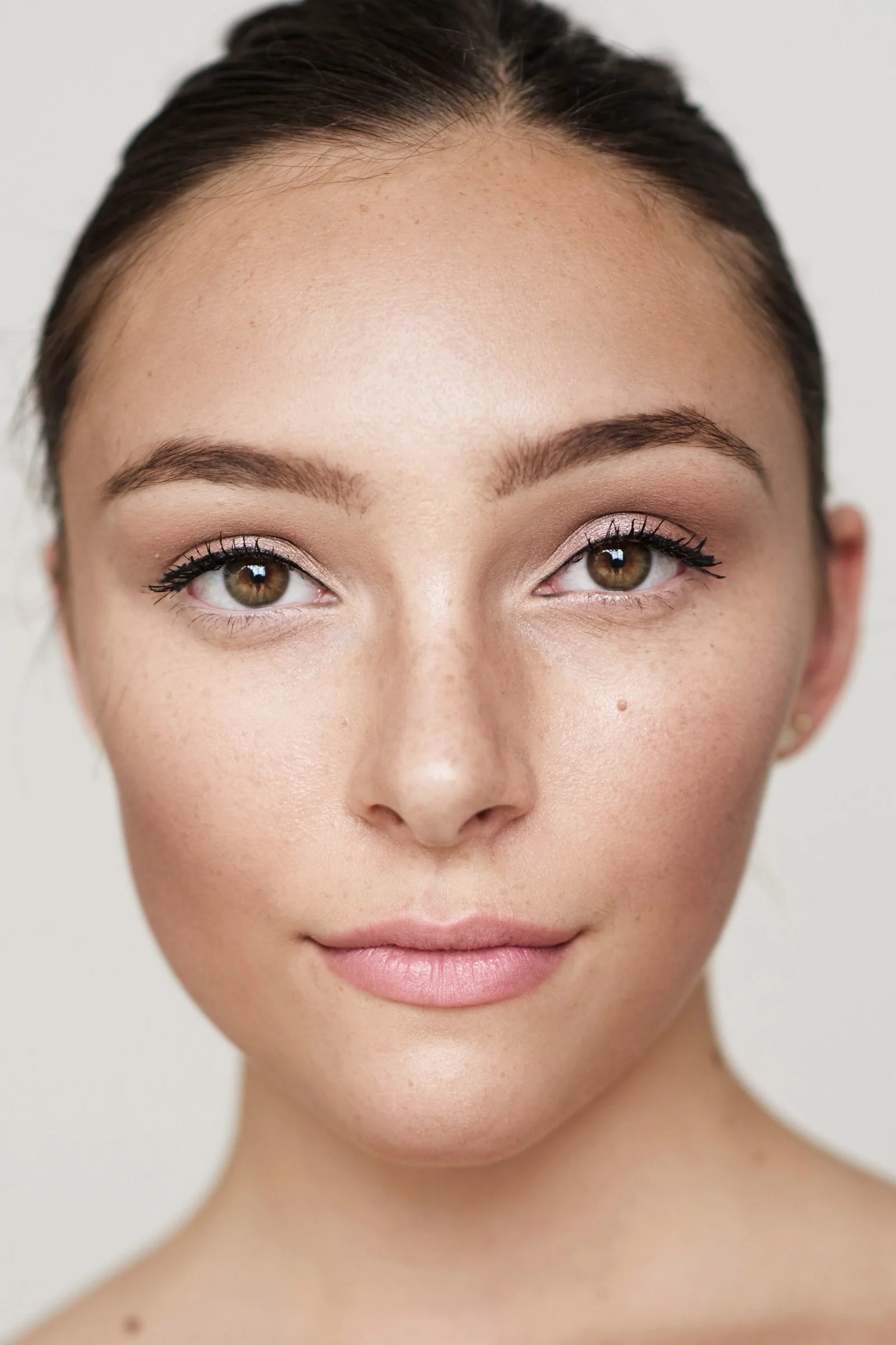 Close-up portrait of a woman with flawless skin, minimal makeup, and brown eyes, looking directly at the camera.