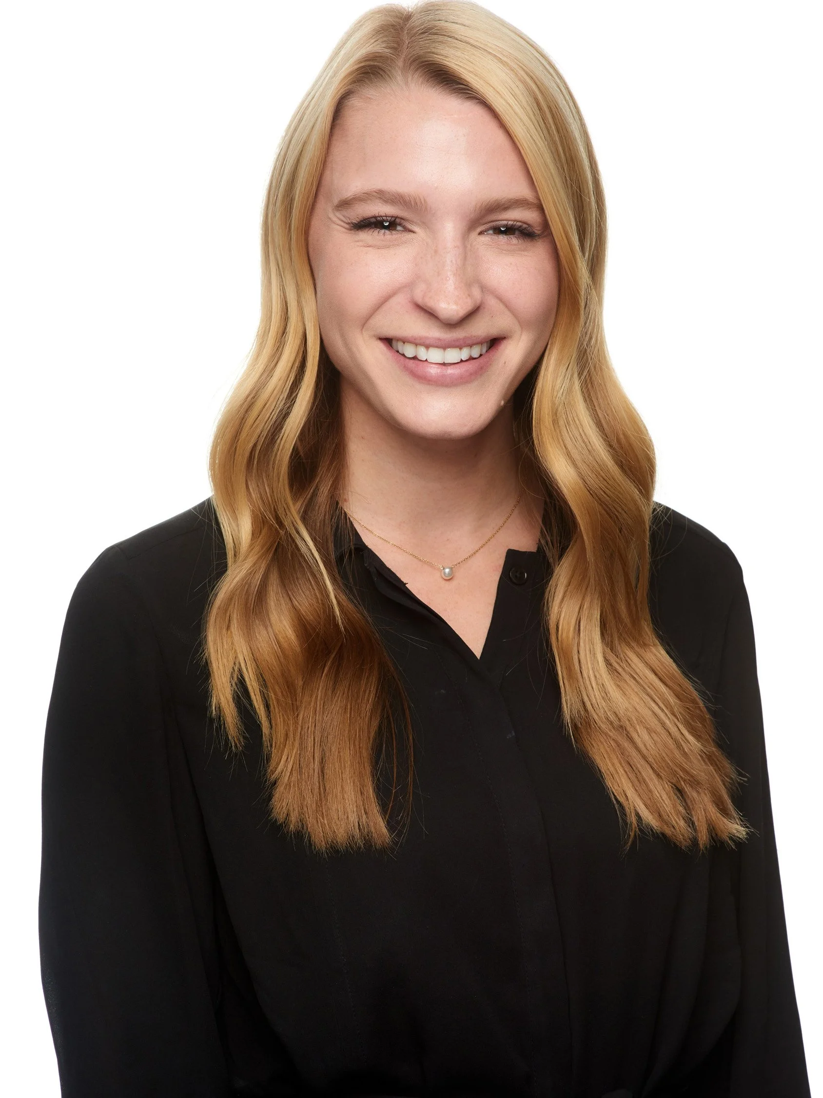 Smile of a young woman with long, wavy, blonde hair wearing a black collared shirt and a delicate necklace.
