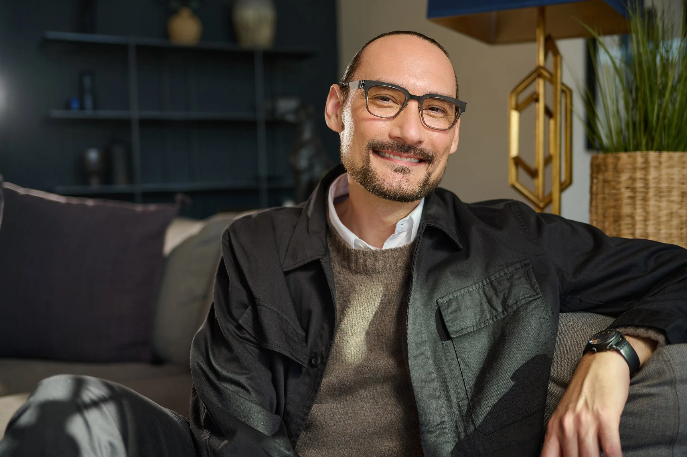 Smiling man with glasses sitting on a beige couch in a modern living room