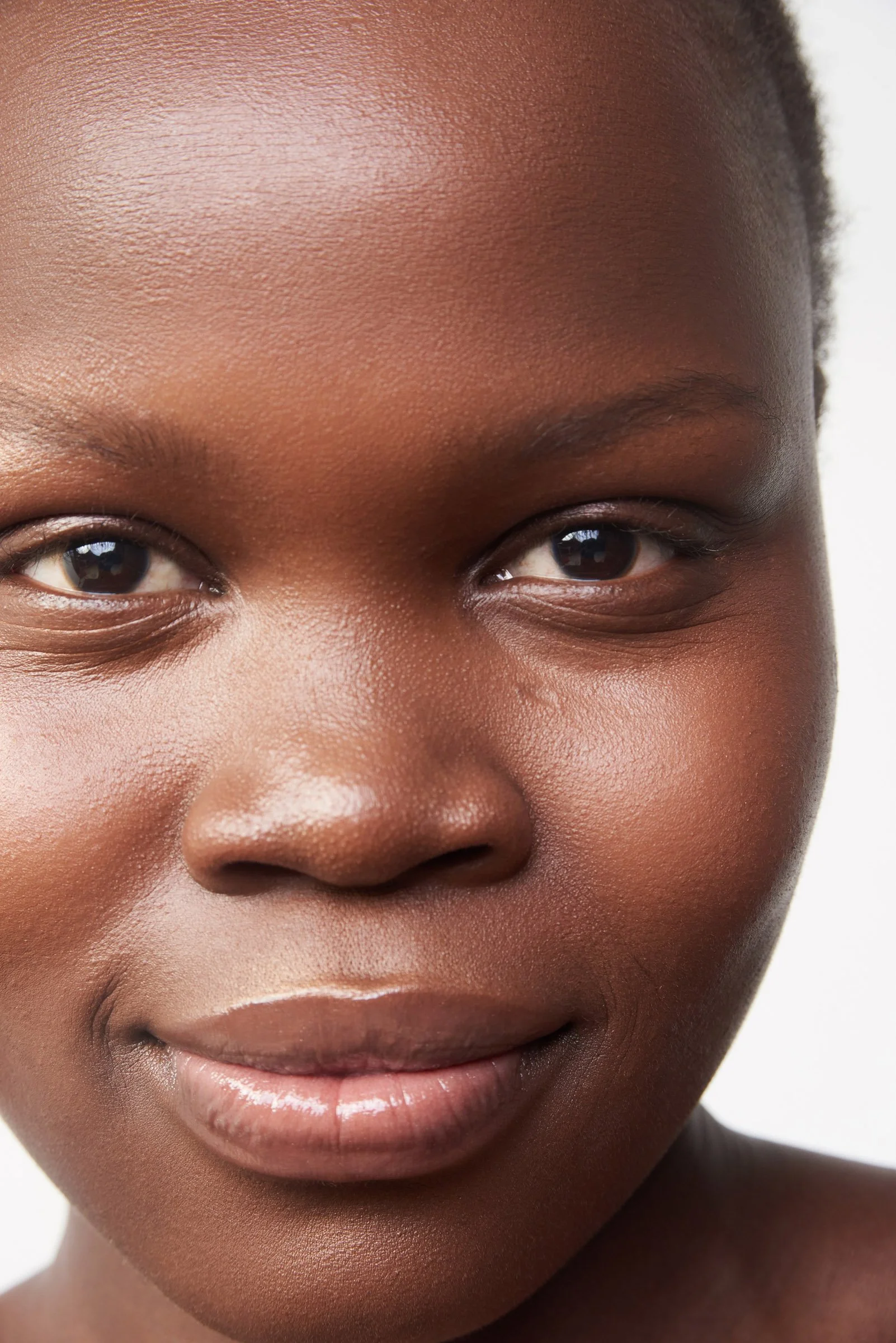 Close-up of a woman with smooth, dark skin, smiling gently, with a white background.