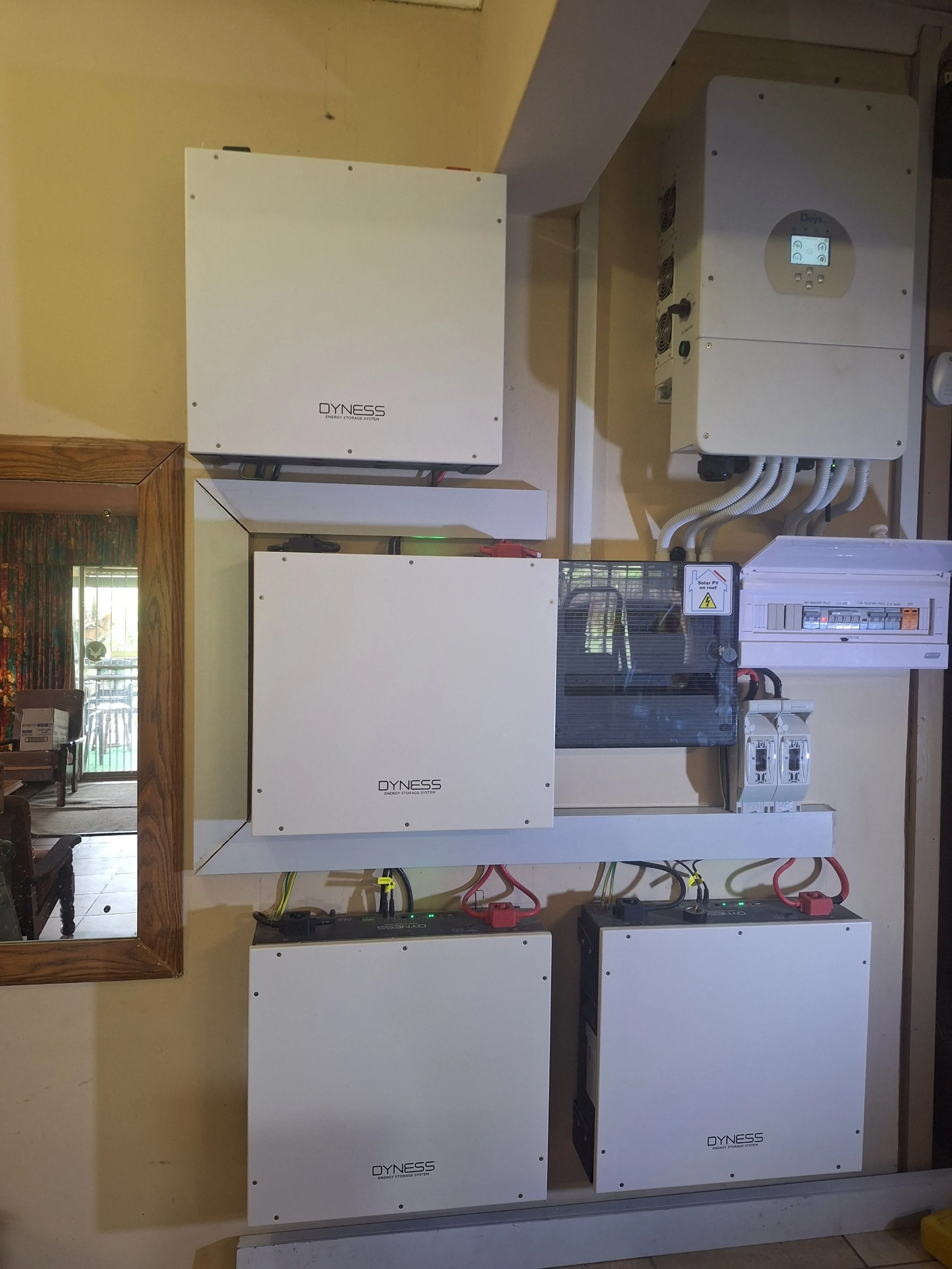 Multiple white energy storage units labeled 'DYNESS' are installed on a beige wall with visible wiring and electrical components.
