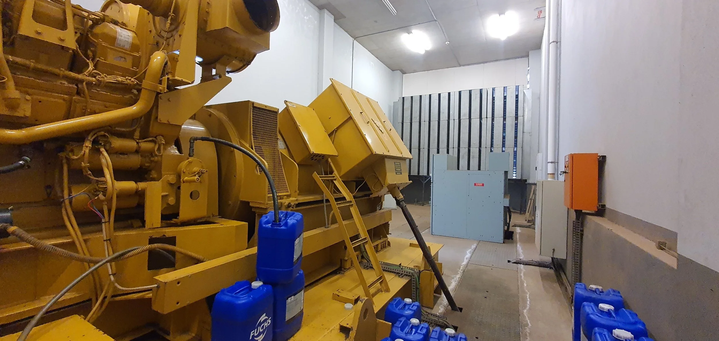 Industrial room with large yellow machinery, blue containers, and electrical panels.