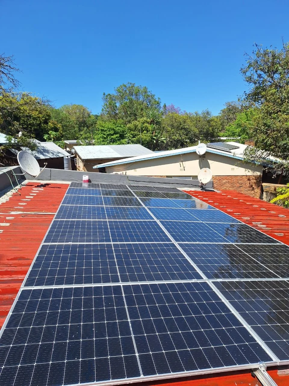 Commercial building roof with multiple solar panels and satellite dishes under clear blue sky.