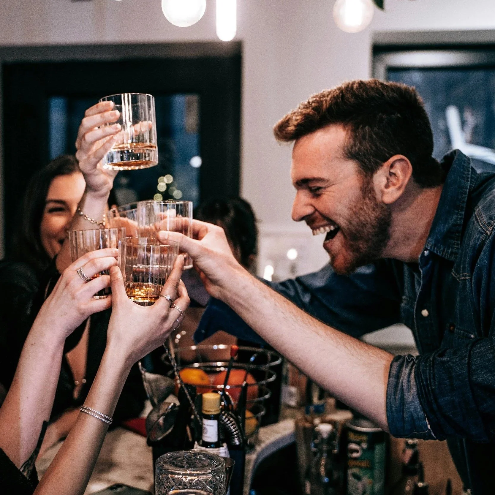 People clinking glasses in a toast at a bar or restaurant, smiling and celebrating.