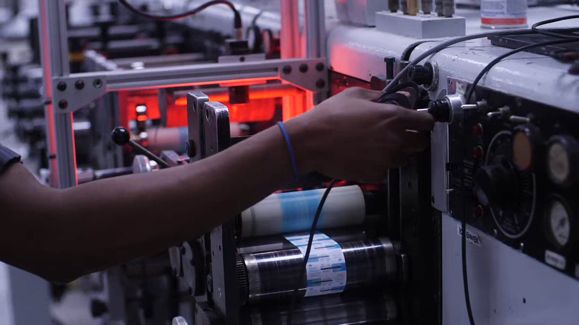 Person's hand operating a machine with rolls of printed material, in an industrial setting.