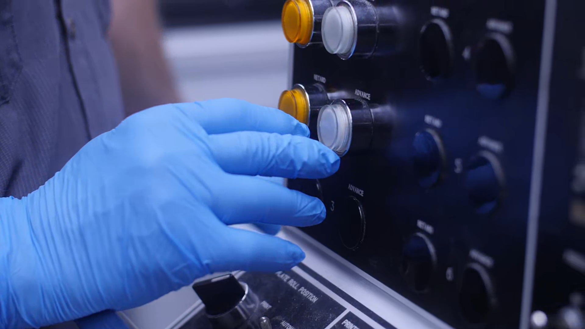 Close-up of a gloved hand turning a knob on a medical or laboratory equipment panel.