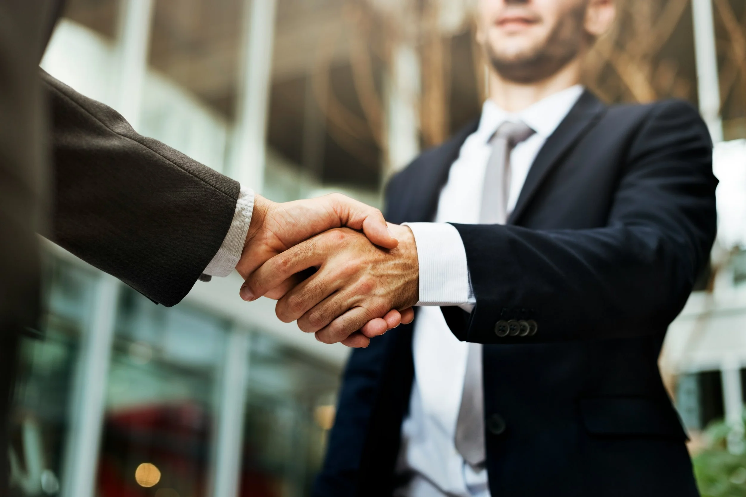 Two men in business suits shaking hands outside a building.