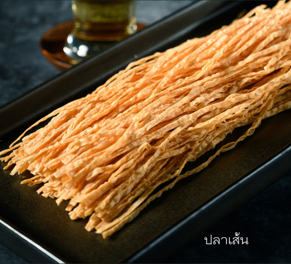 Dried fish strips on a black platter with a drink in the background.