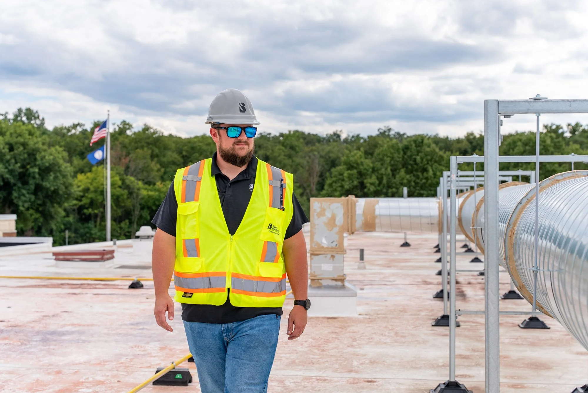 A Blauch Brothers technician walks the rooftop of Sandy Hook Elementary School past rows of new ductwork supports, with American and Virginia flags flying nearby.