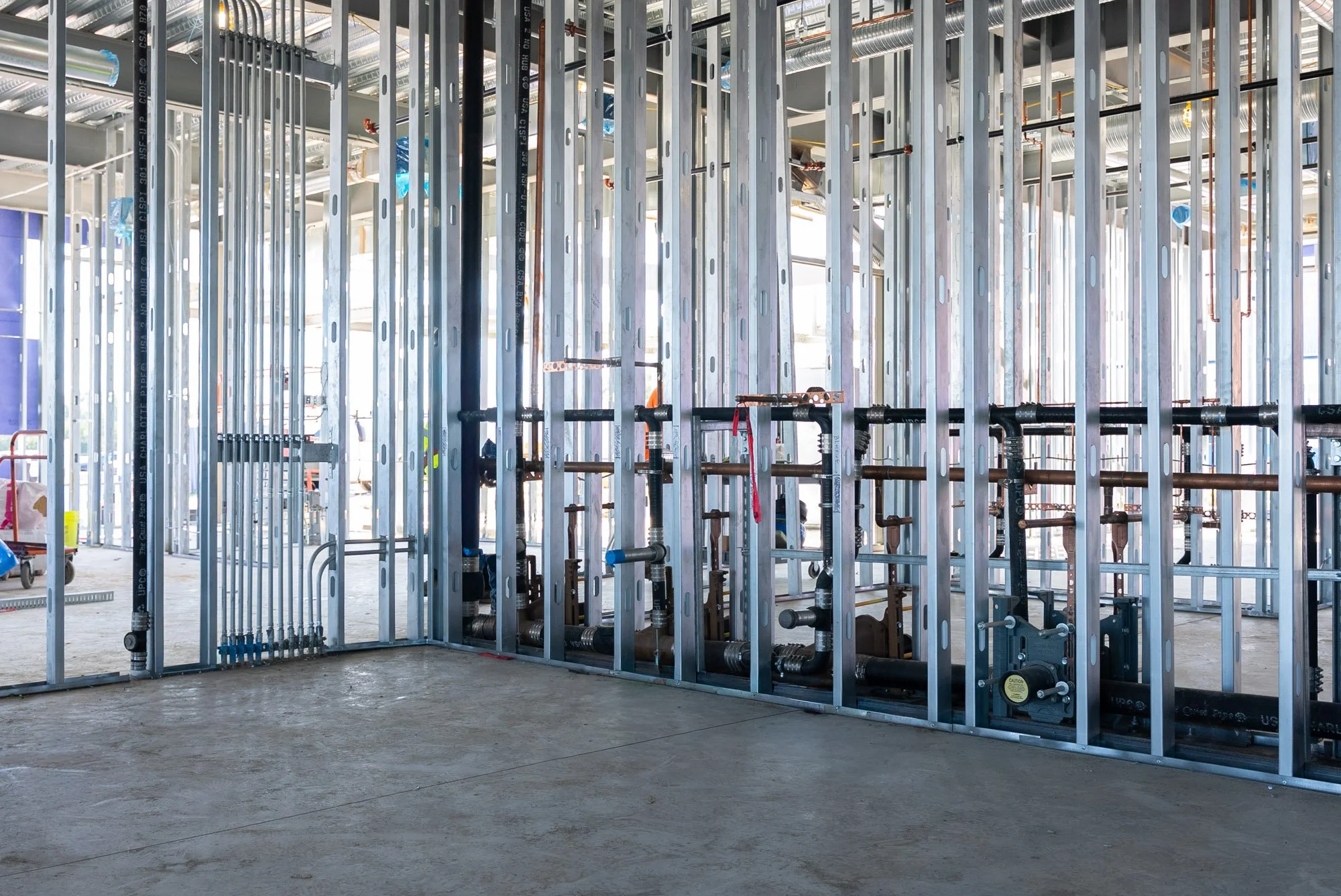 Commercial plumbing rough-in inside metal stud walls at the Daikin Applied office building in Verona, VA, with cast iron drain lines and copper piping set before the walls are closed up.