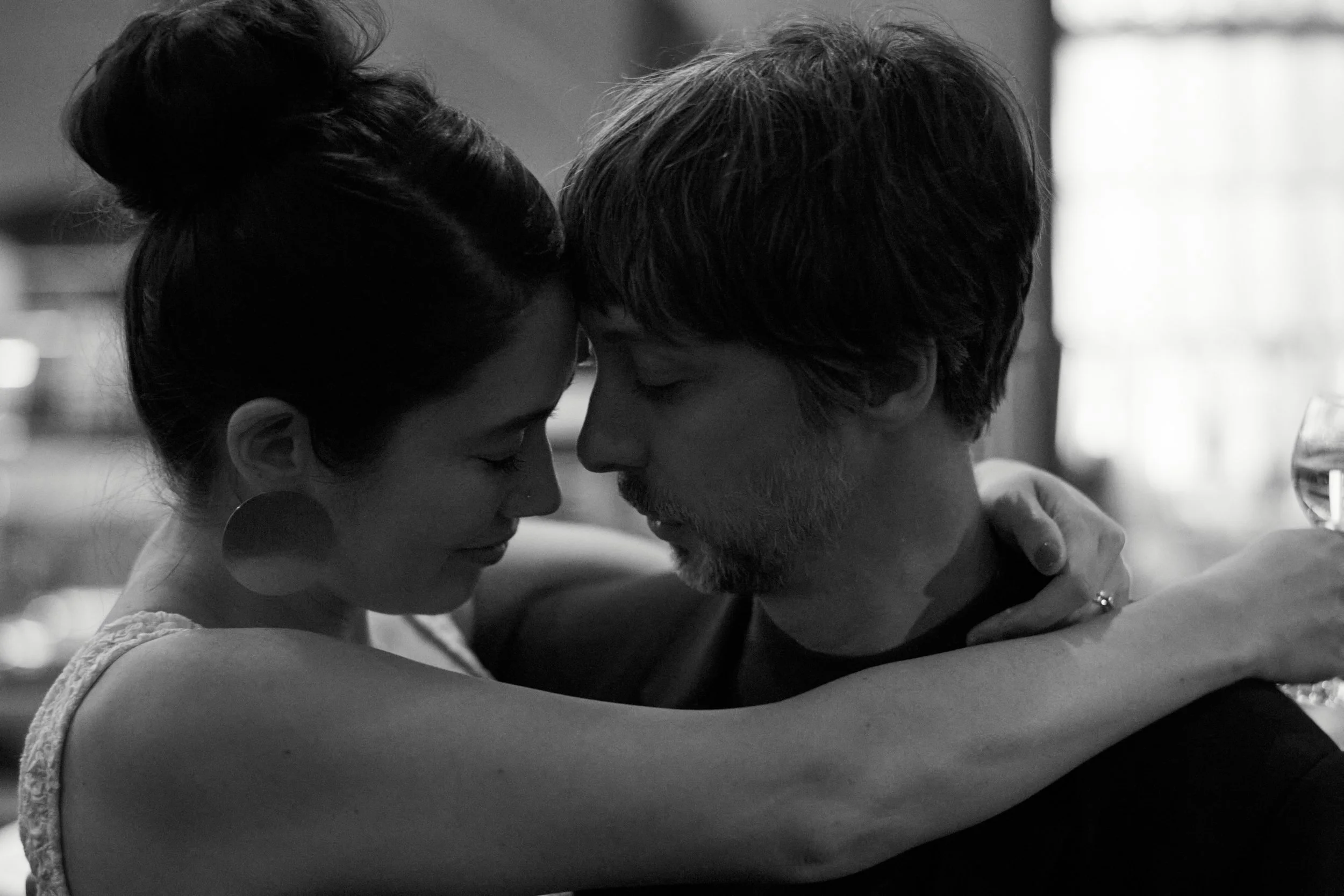 A black and white photo of a couple with foreheads touching, eyes closed, embracing each other intimately.