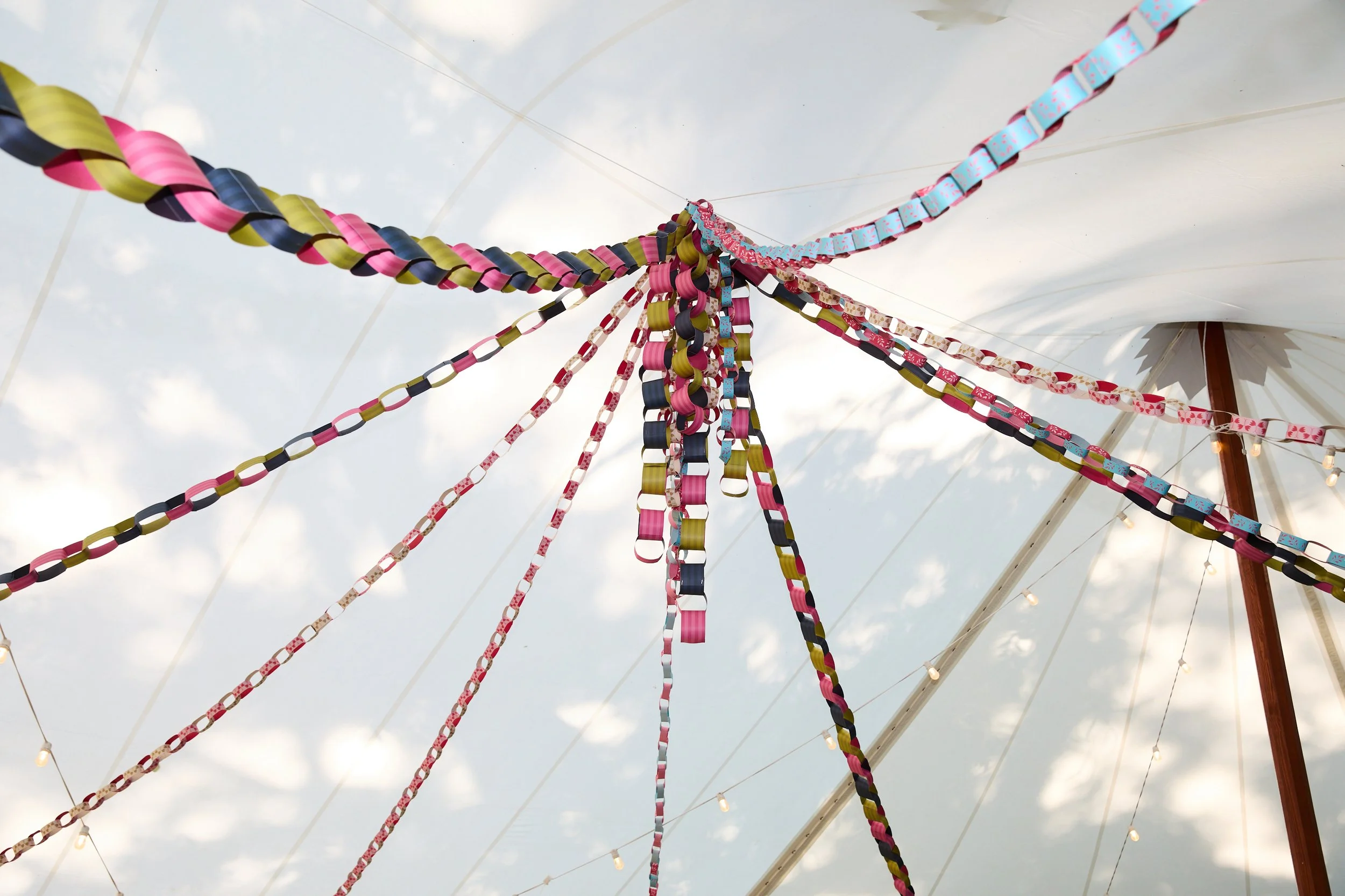 Colorful ribbons hanging from a central point under a white canopy with string lights, looking up at the sky.