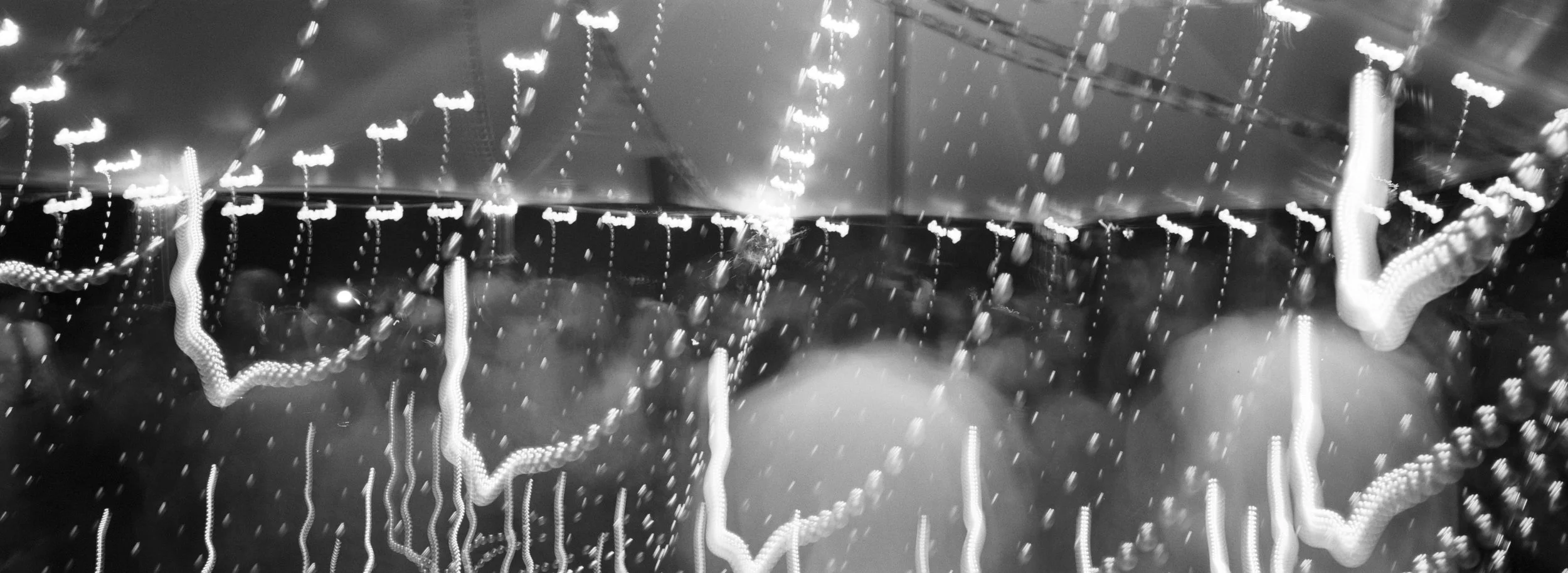 A black-and-white photo of a carnival ride with hanging lights and chains, creating a blurred, streaked effect.
