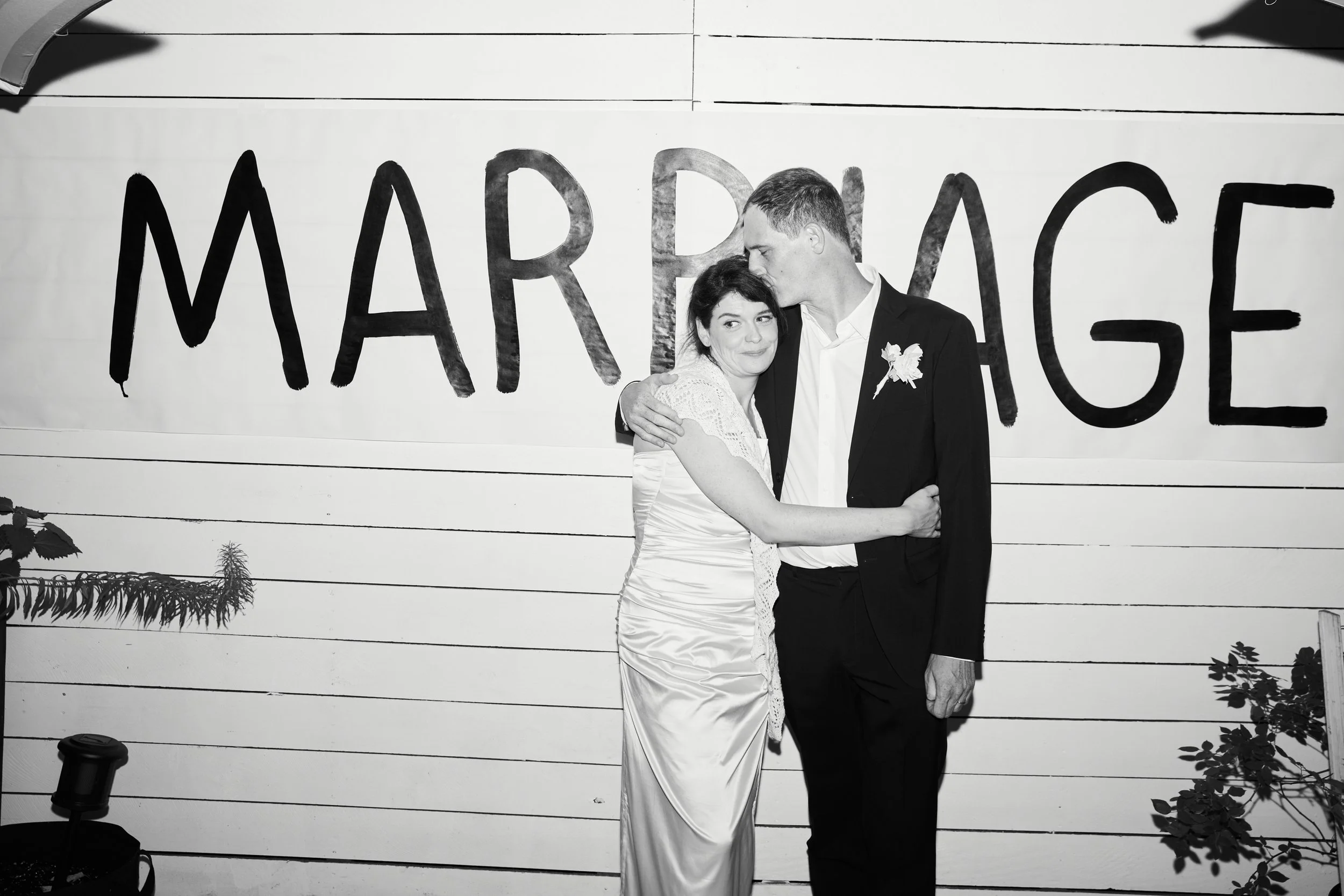 A couple hugging in front of a sign that says 'Marriage' at their wedding.