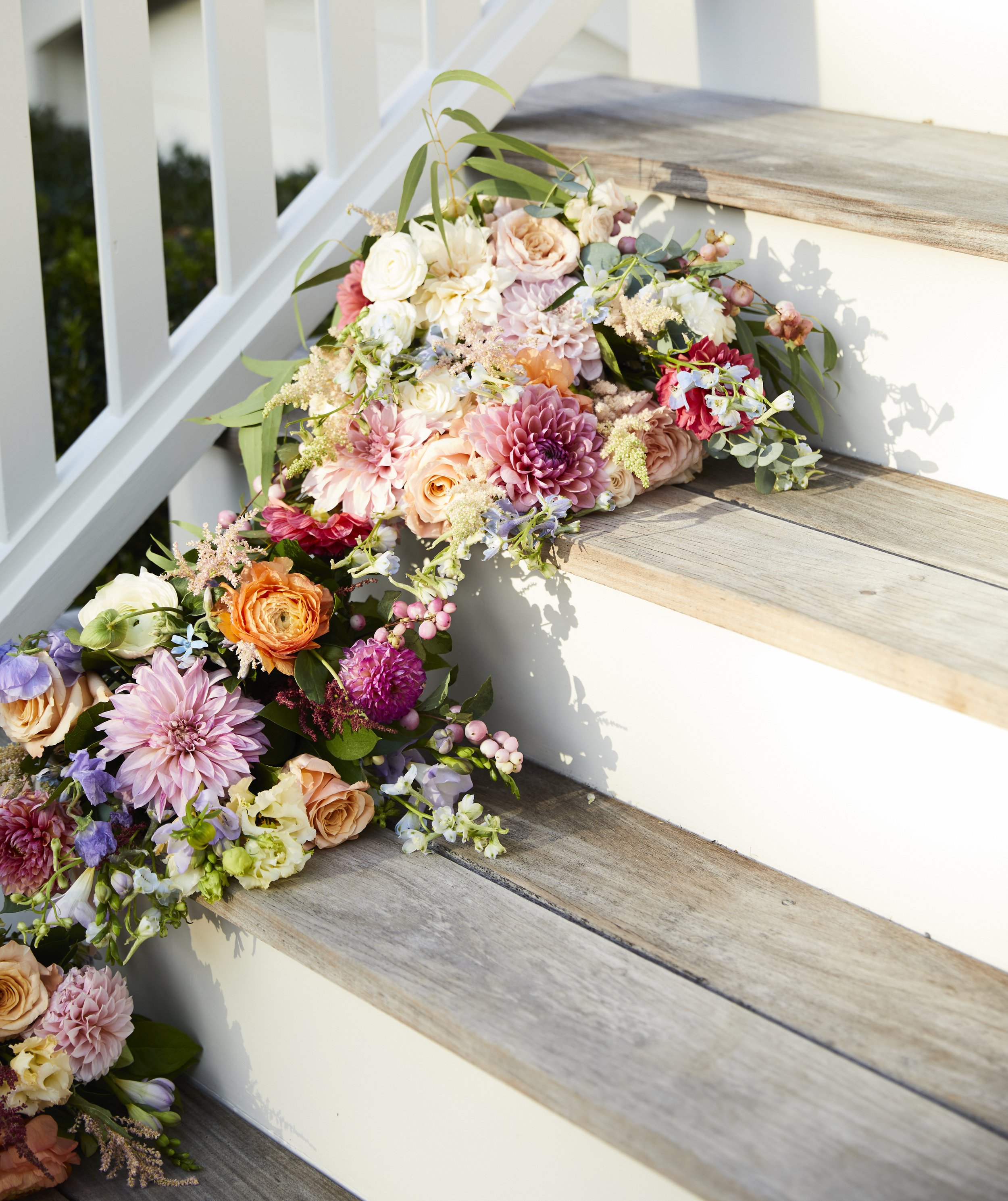 A bouquet of colorful flowers, including roses and dahlias, arranged on wooden stairs.