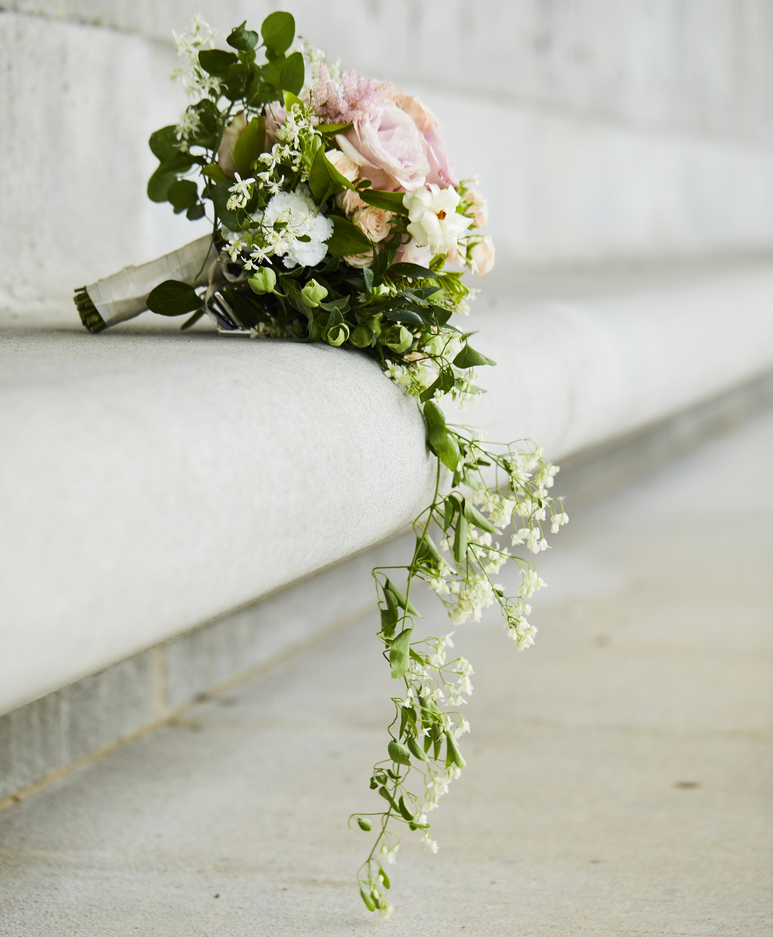A pink and white bridal bouquet with greenery and cascading flowers resting on a light-colored stone ledge.