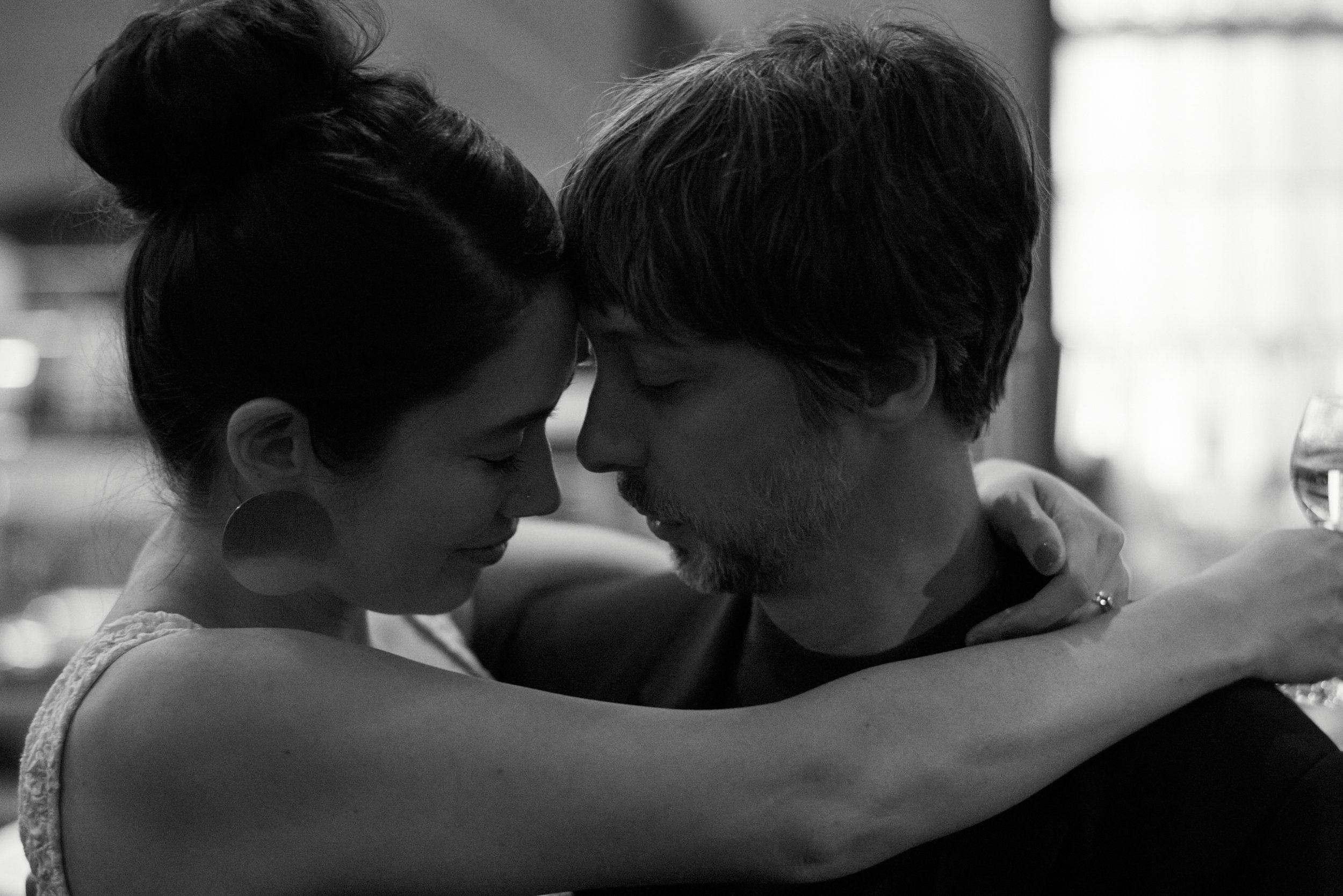 A black and white photo of a couple embracing closely with foreheads touching and eyes closed, creating an intimate moment.
