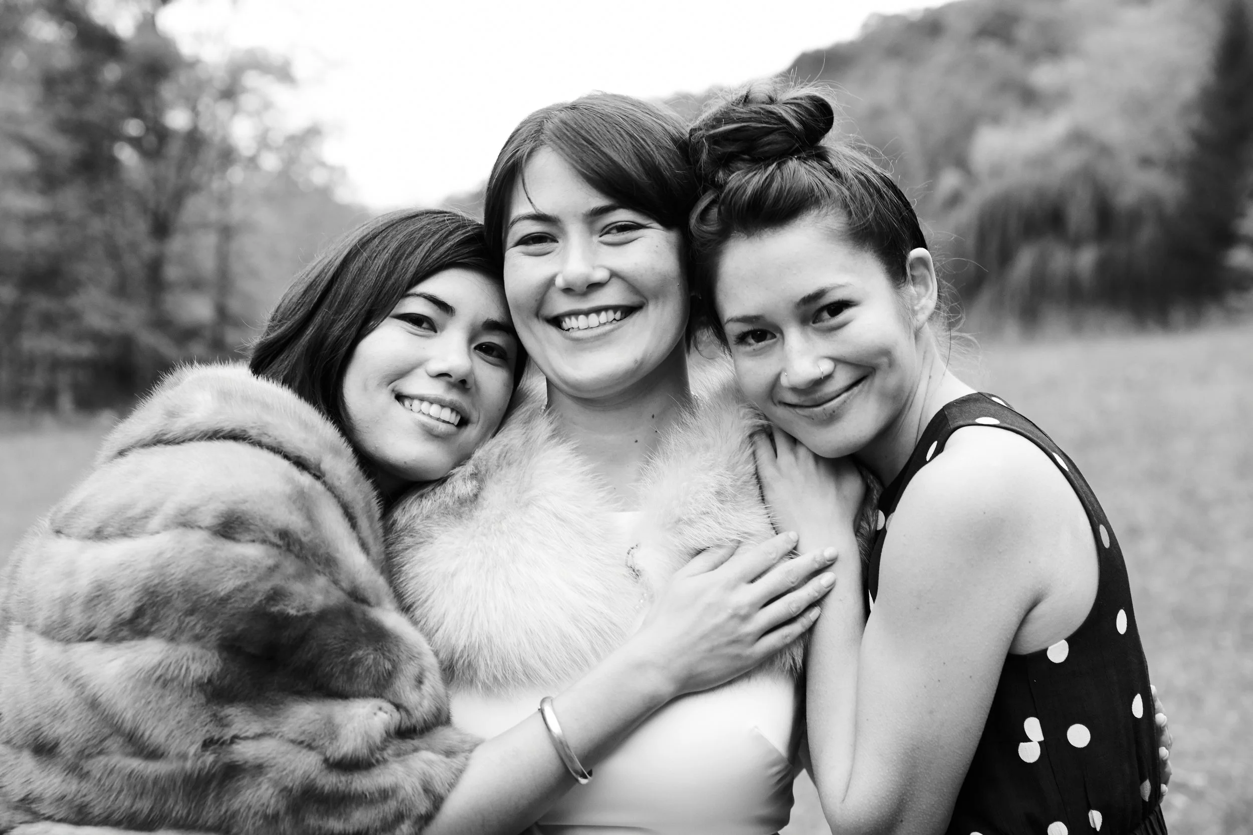 Three women smiling and hugging outdoors in black and white.