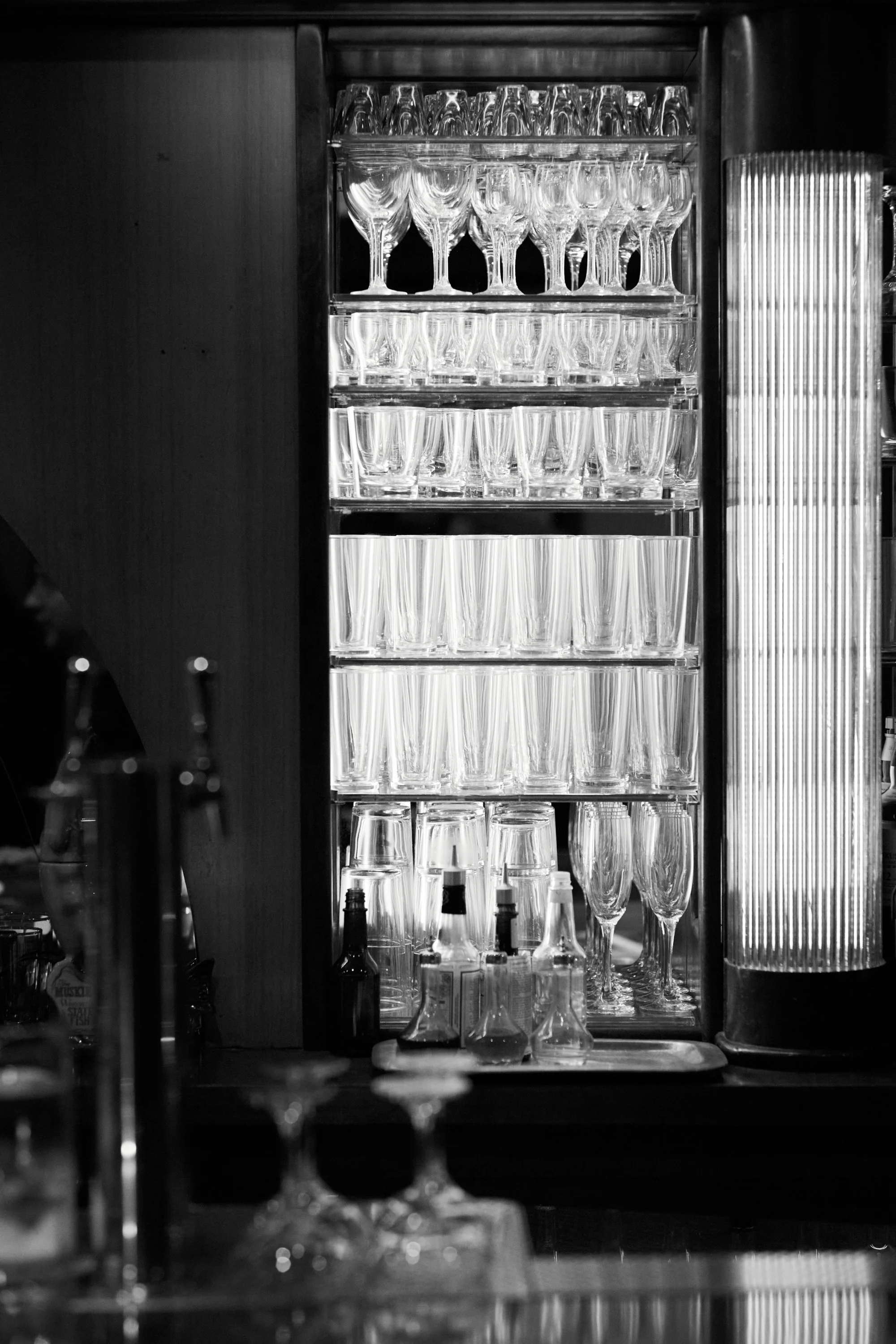 Shelves with various glassware including wine glasses, champagne flutes, and shot glasses in a bar or restaurant setting.