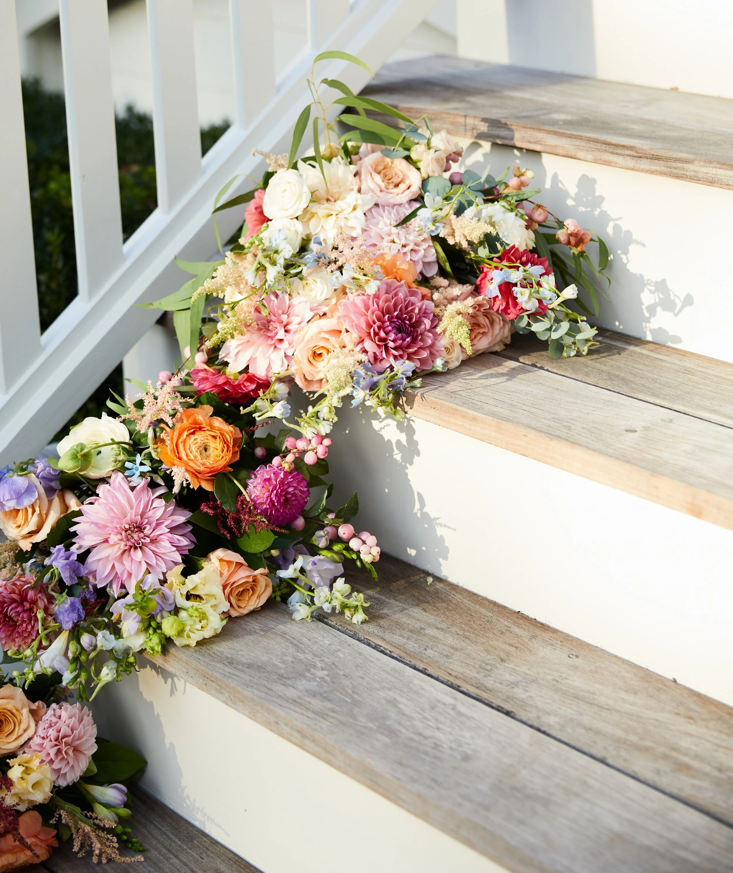 Colorful flower arrangement decorated along wooden steps and white railing.