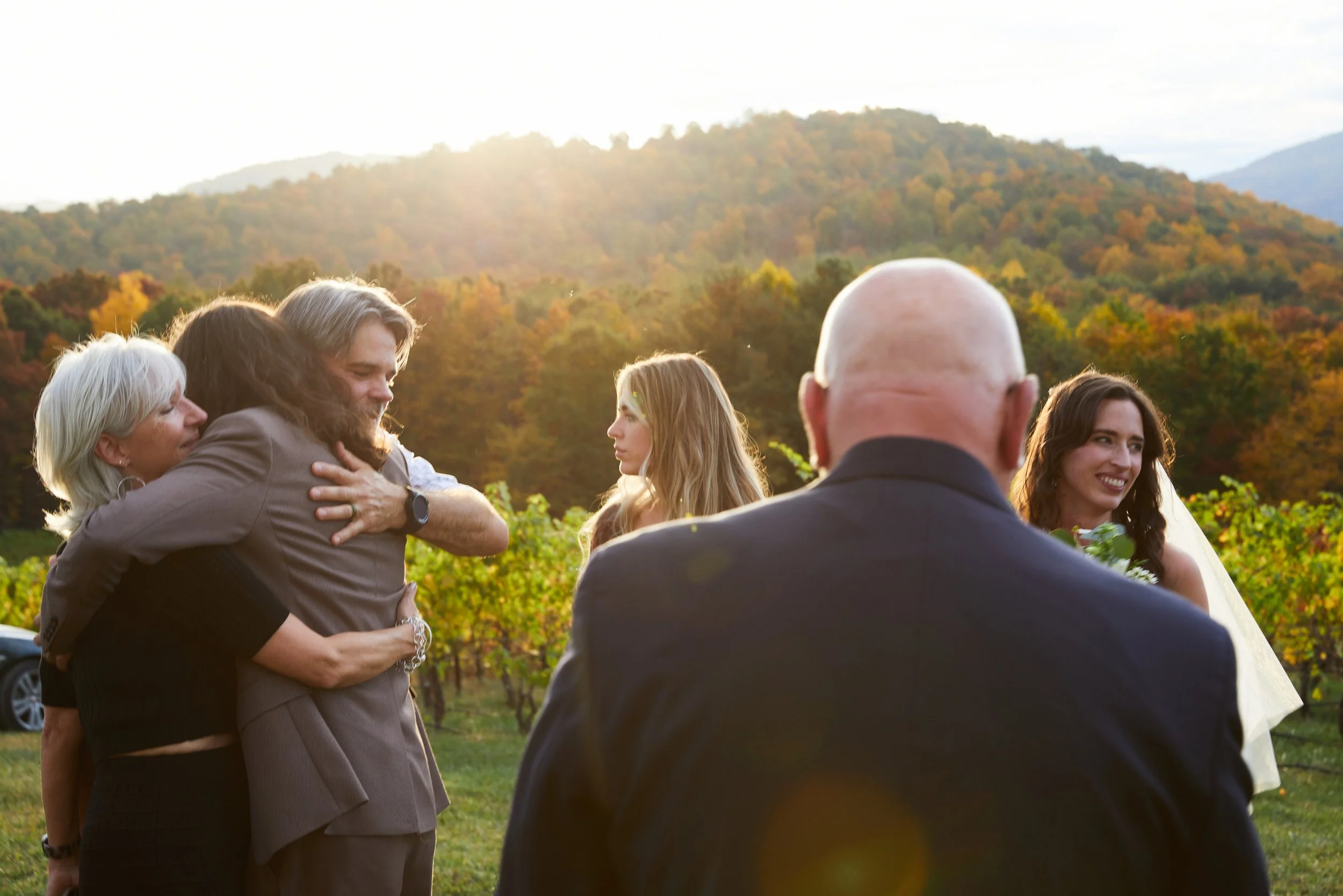 People embracing outdoors during sunset with mountains and trees in the background.