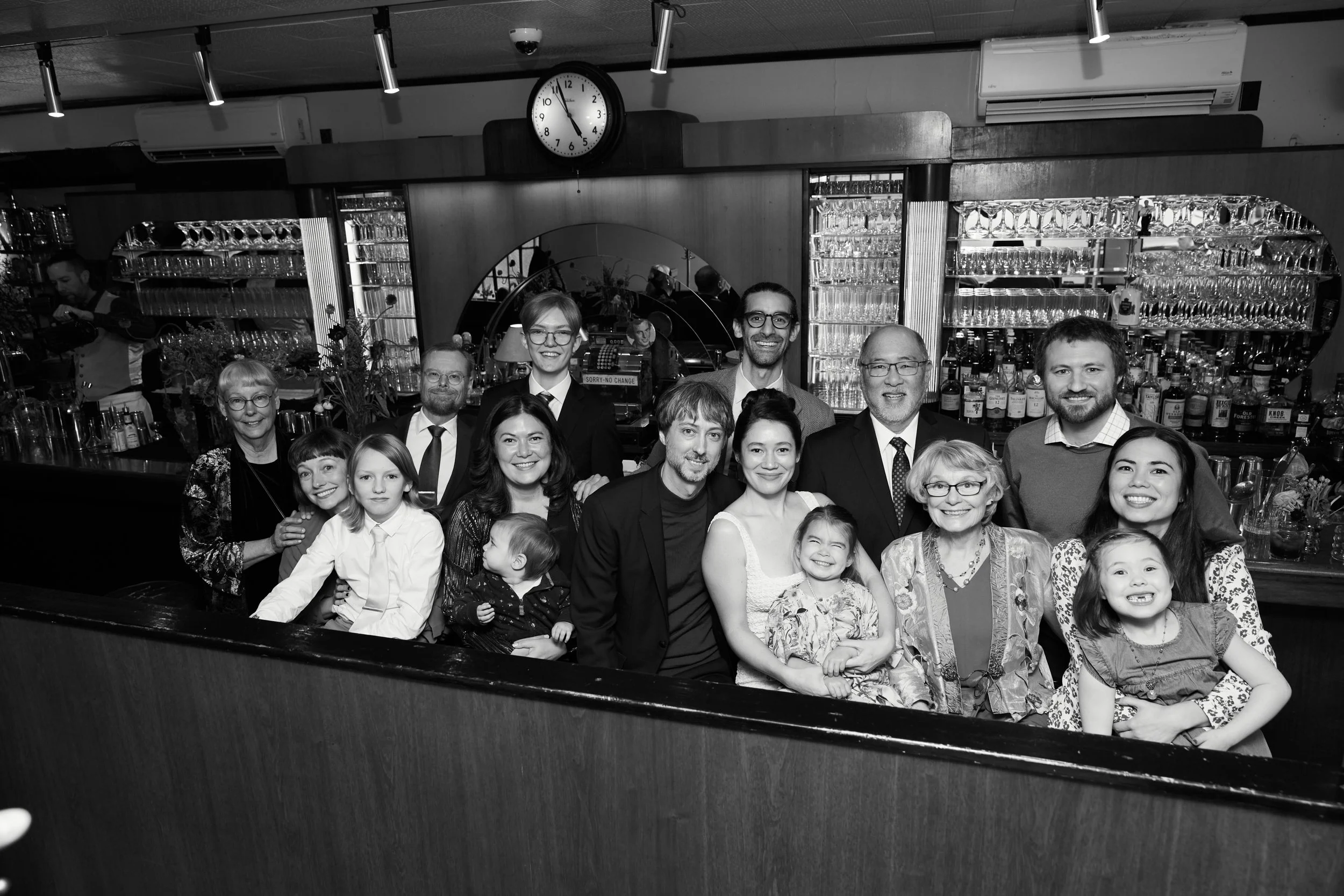 A group of adults and children posing together in a restaurant or bar, smiling for a photo.
