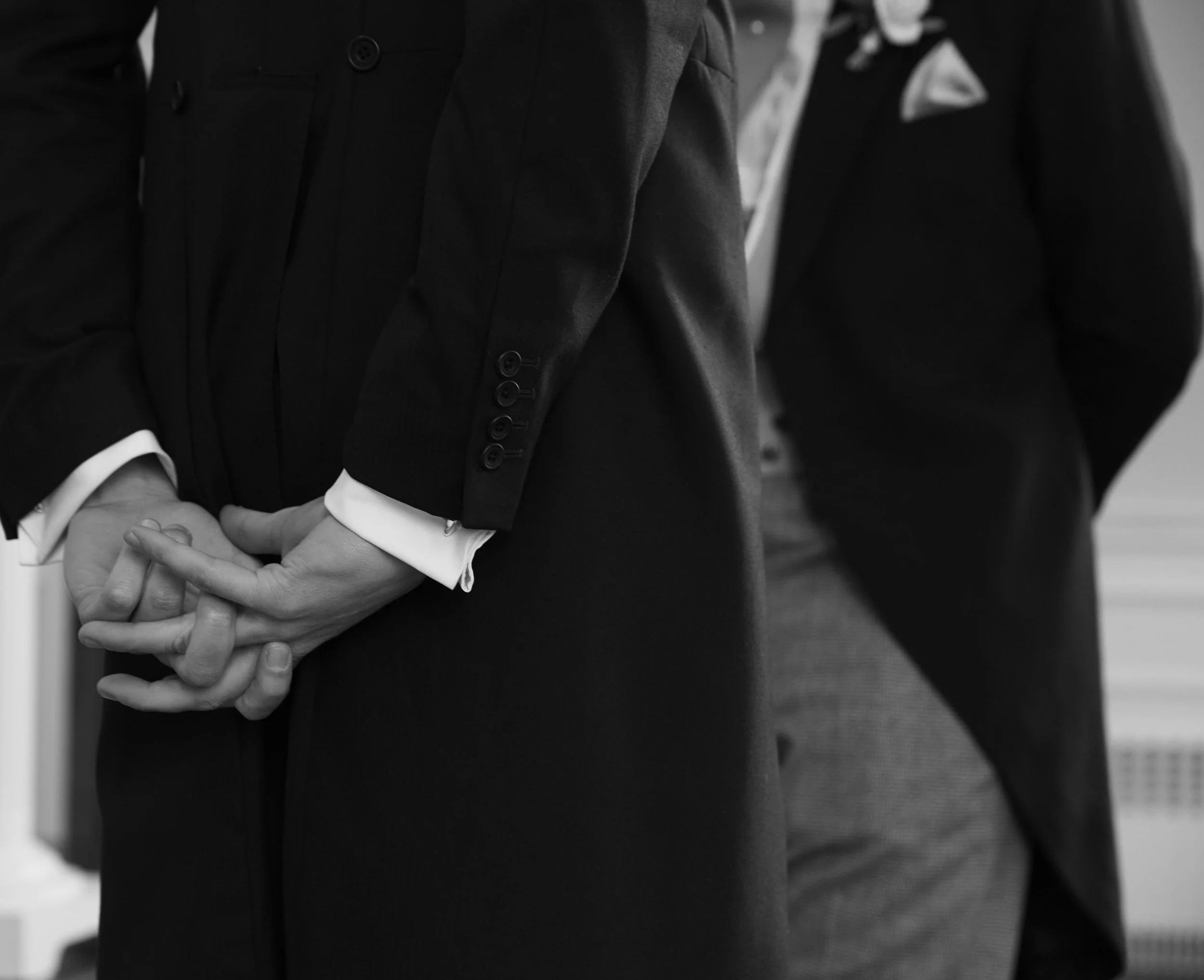 Two men in suits standing face to face, holding hands in a firm handshake.