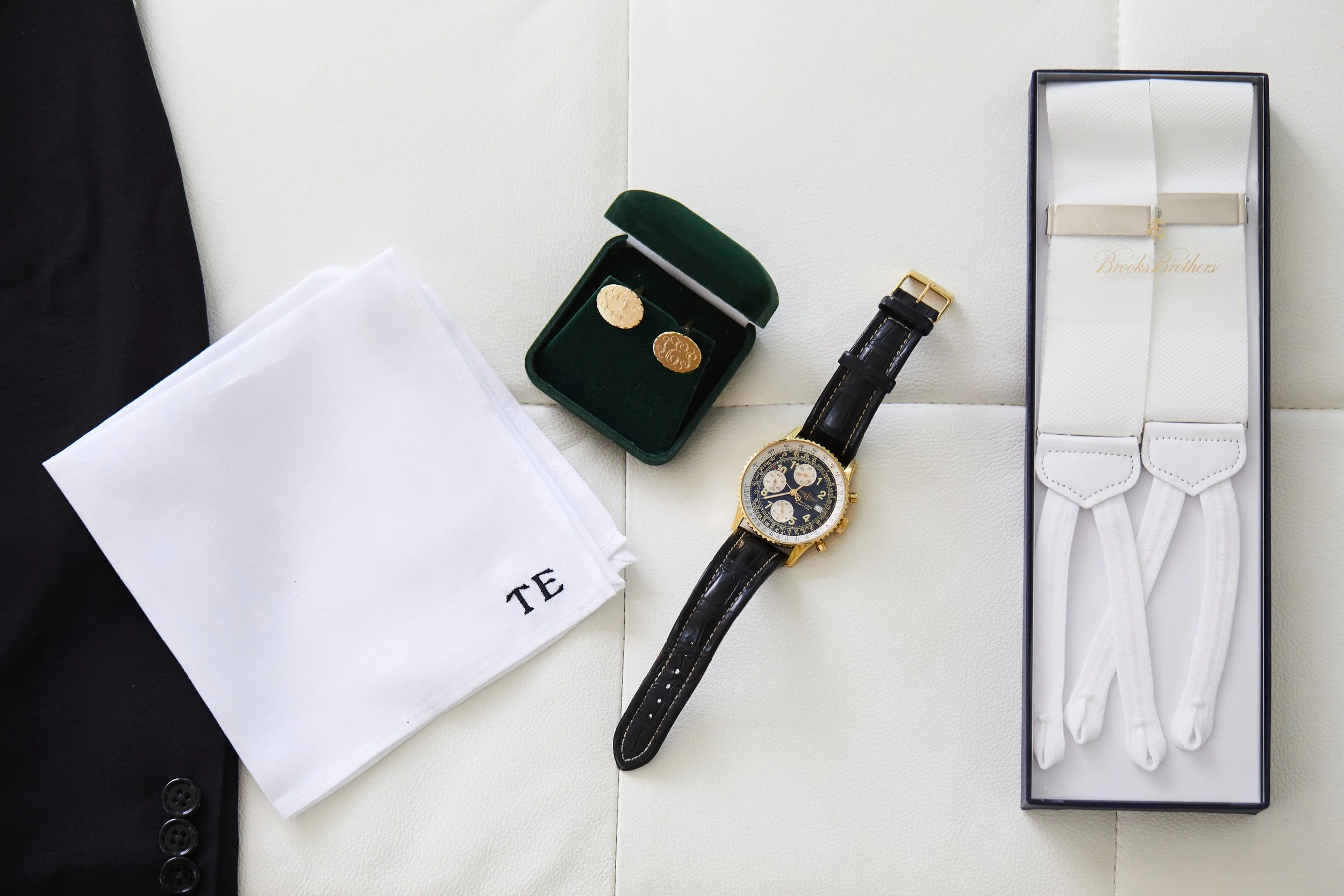 Watch, cufflinks, suspenders, cleaning cloth, and box on white surface.