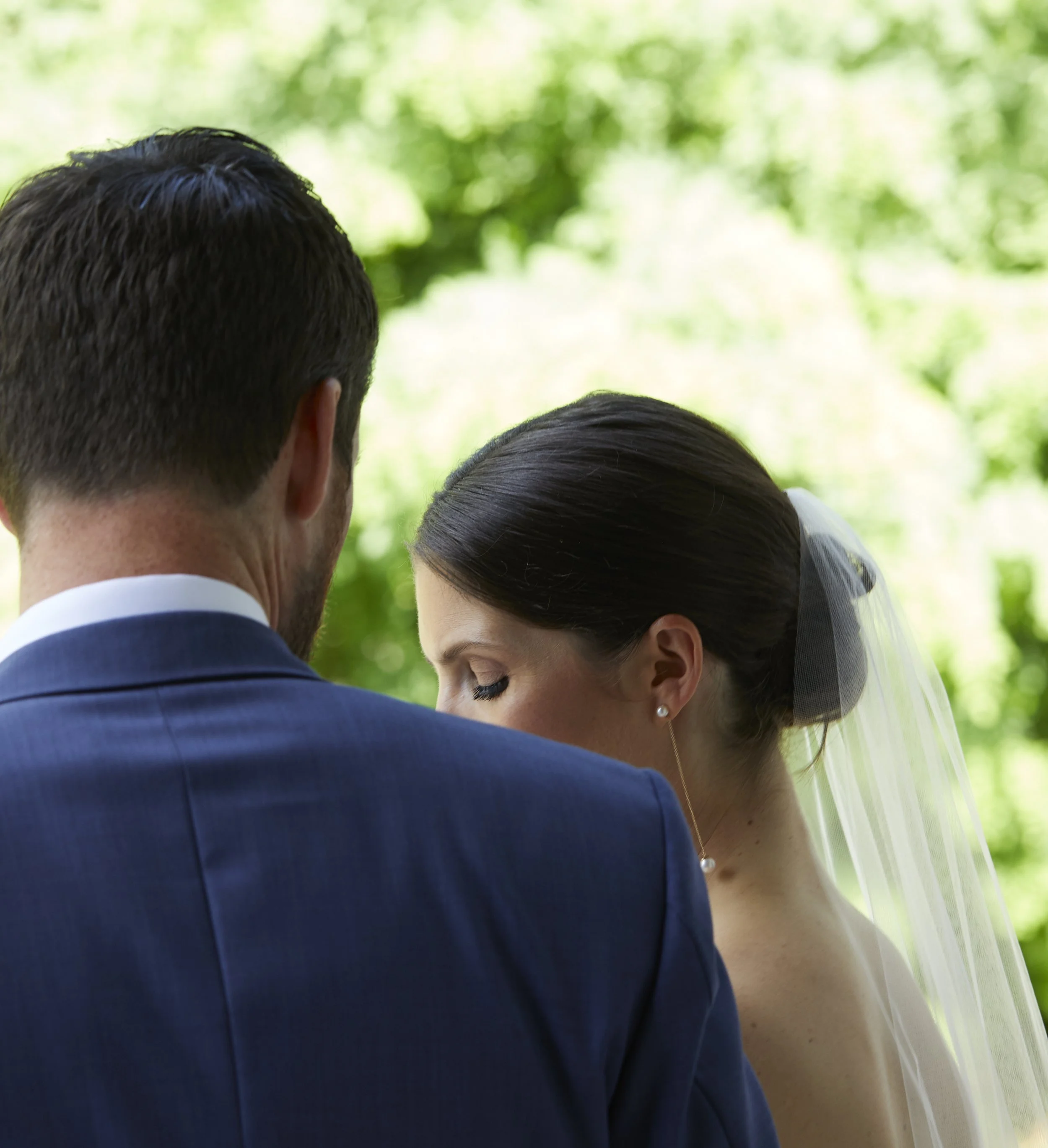 A bride and groom sharing an intimate moment outdoors during their wedding, with greenery in the background.