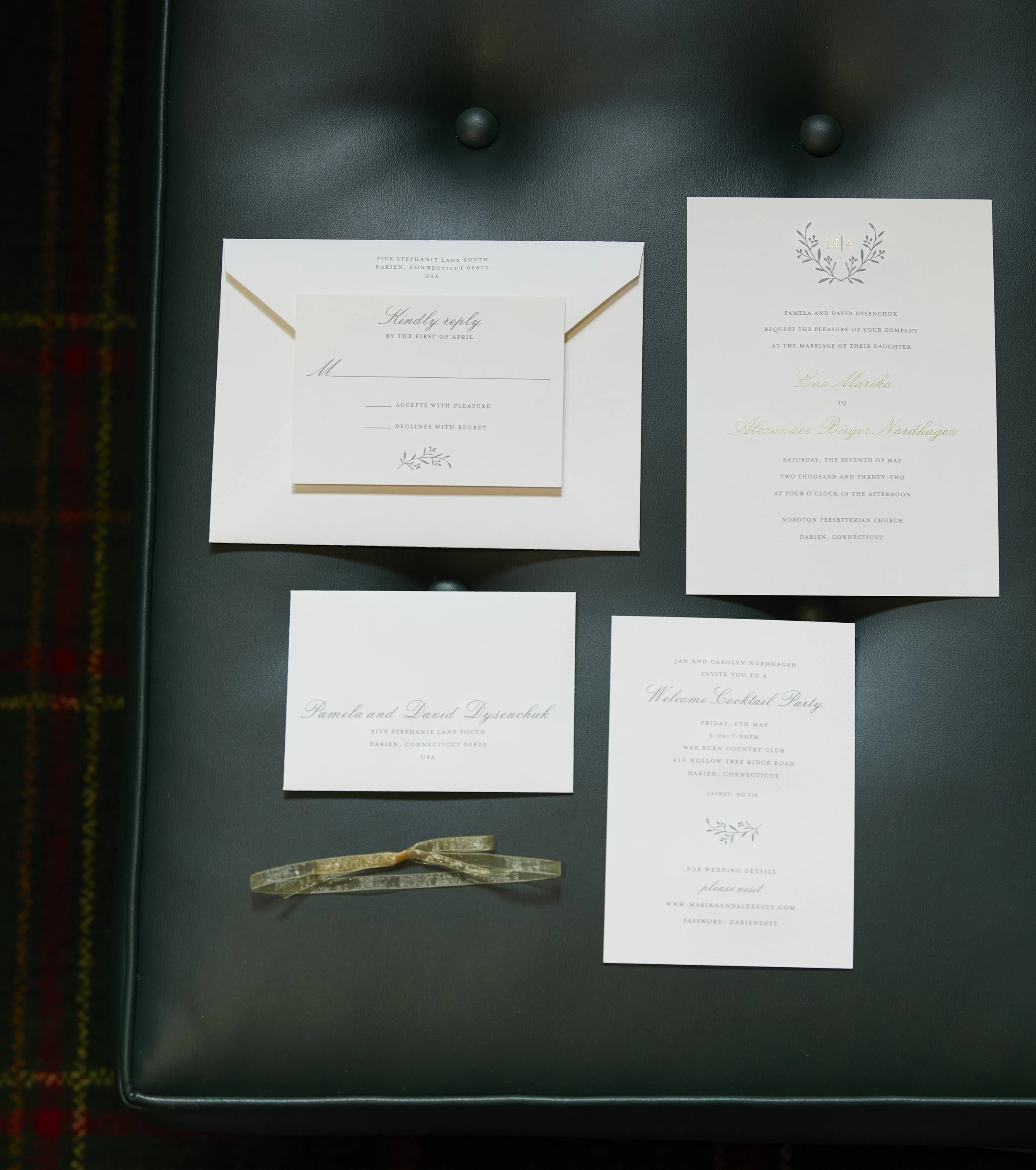 Wedding invitation suite including a main invitation, rsvp card, envelope, and details card, all with a minimalistic design and floral accents, placed on a black surface.