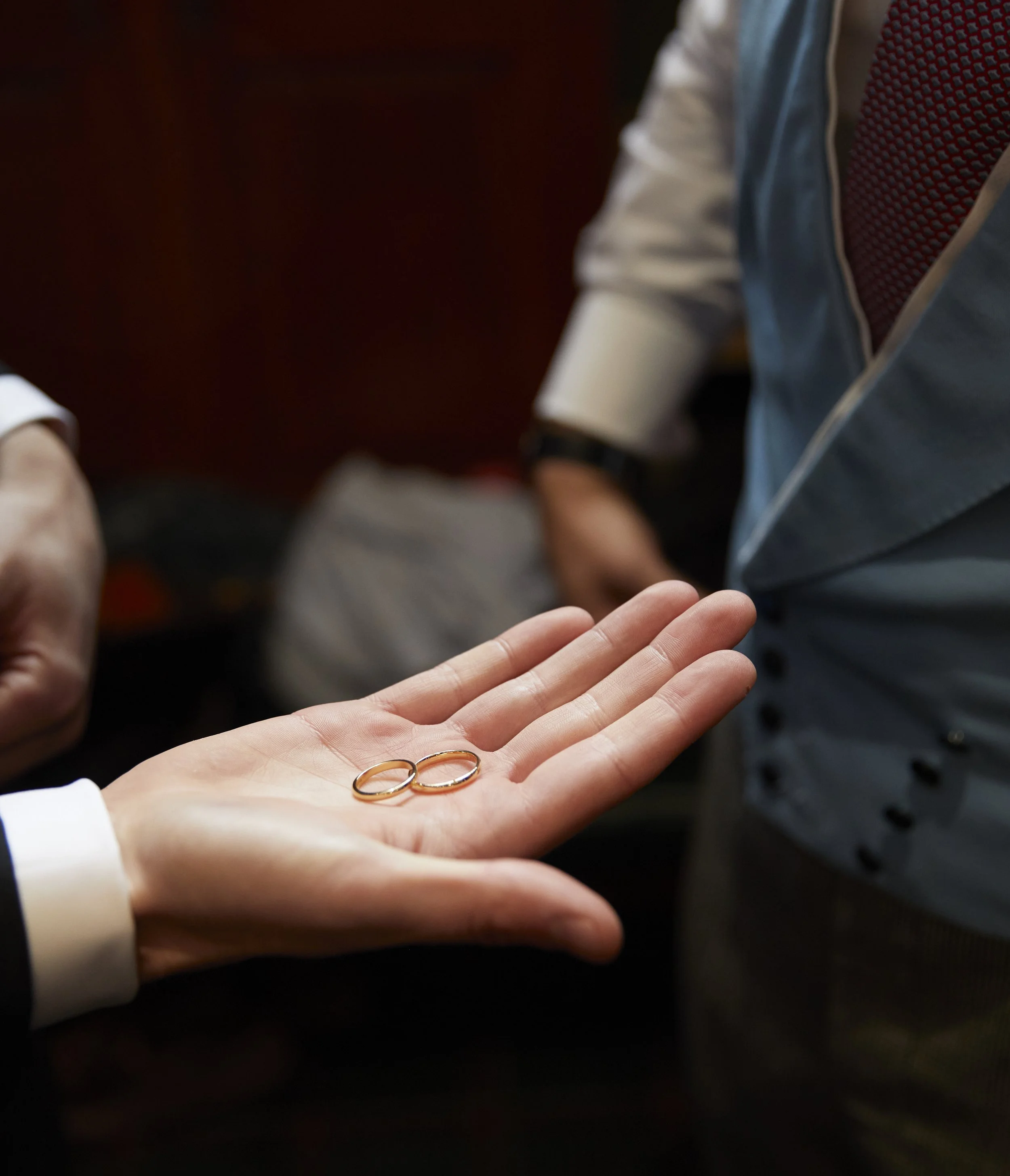 Person holding two wedding rings, with other person in the background.