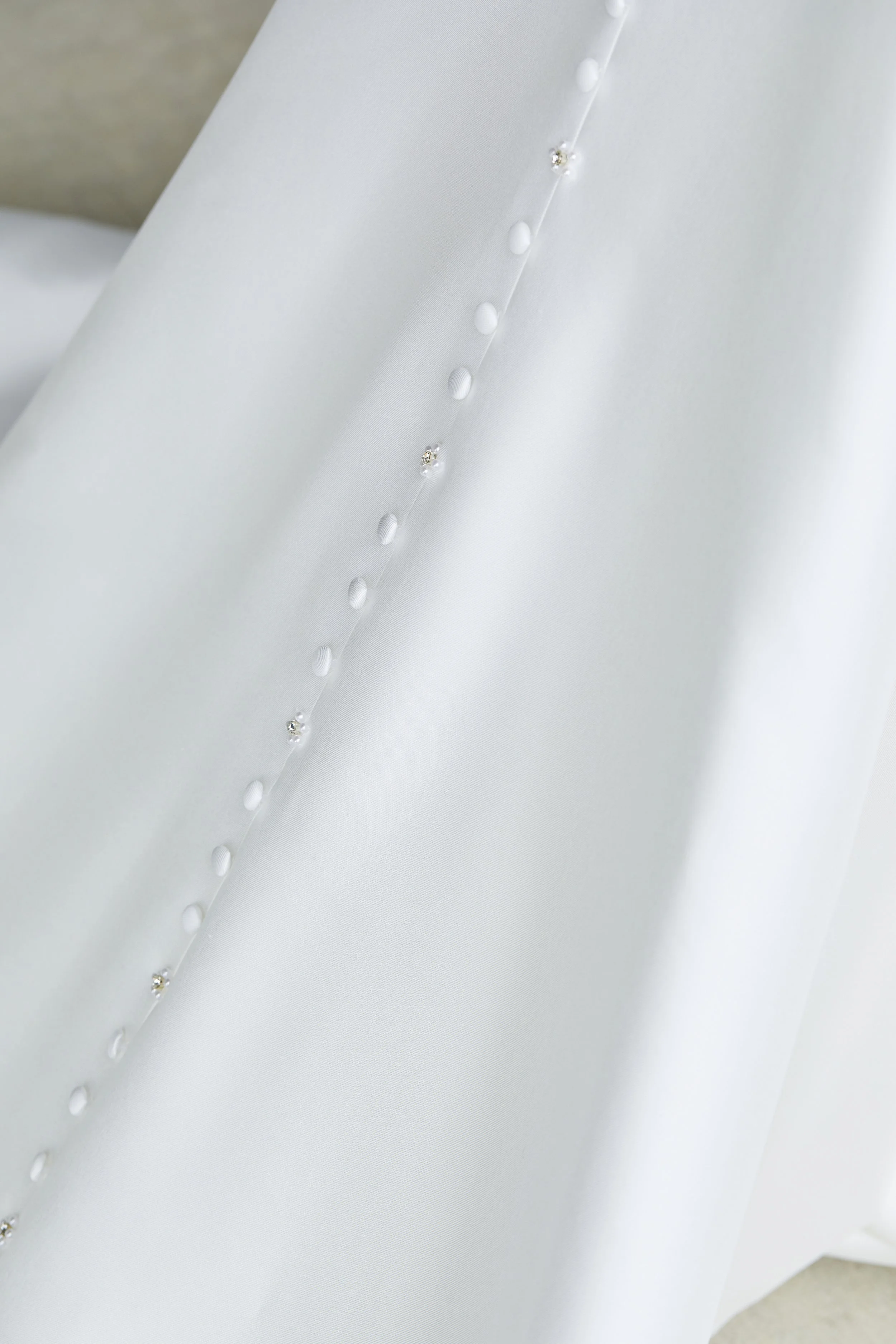 Close-up of a white satin or silk fabric with small pearl-like beads and tiny rhinestones or crystals arranged in a line.